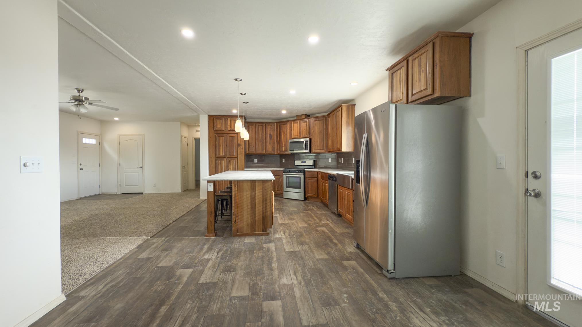Kitchen with stainless steel appliances, a center island, brown cabinets, light countertops, and pendant lighting