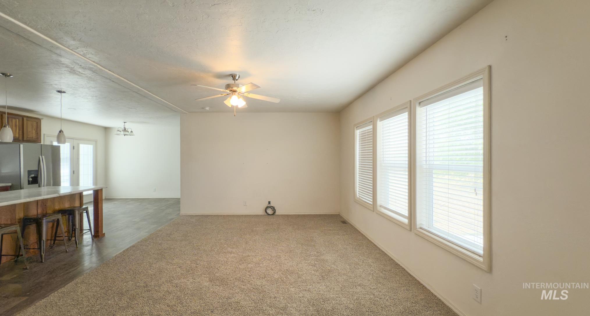 Unfurnished living room featuring dark carpet, a textured ceiling, and a ceiling fan