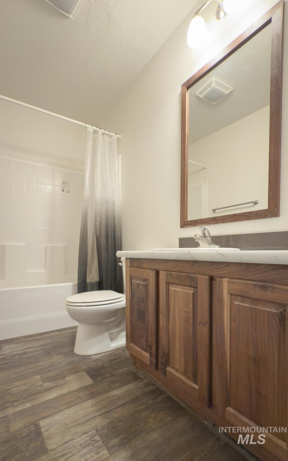 Bathroom with shower / bath combination with curtain, vanity, and dark wood-type flooring