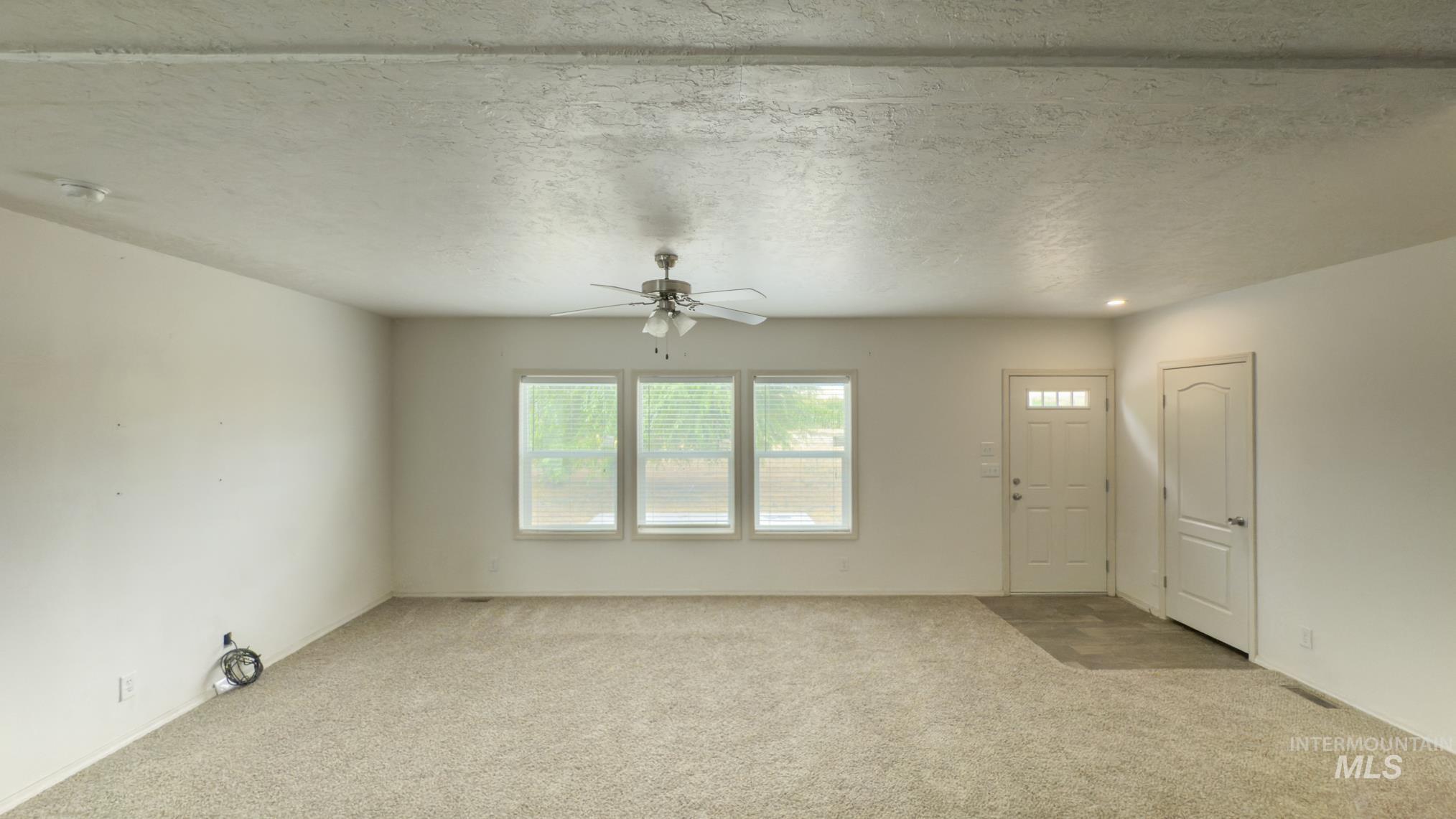 Unfurnished living room featuring a textured ceiling, carpet floors, and a ceiling fan