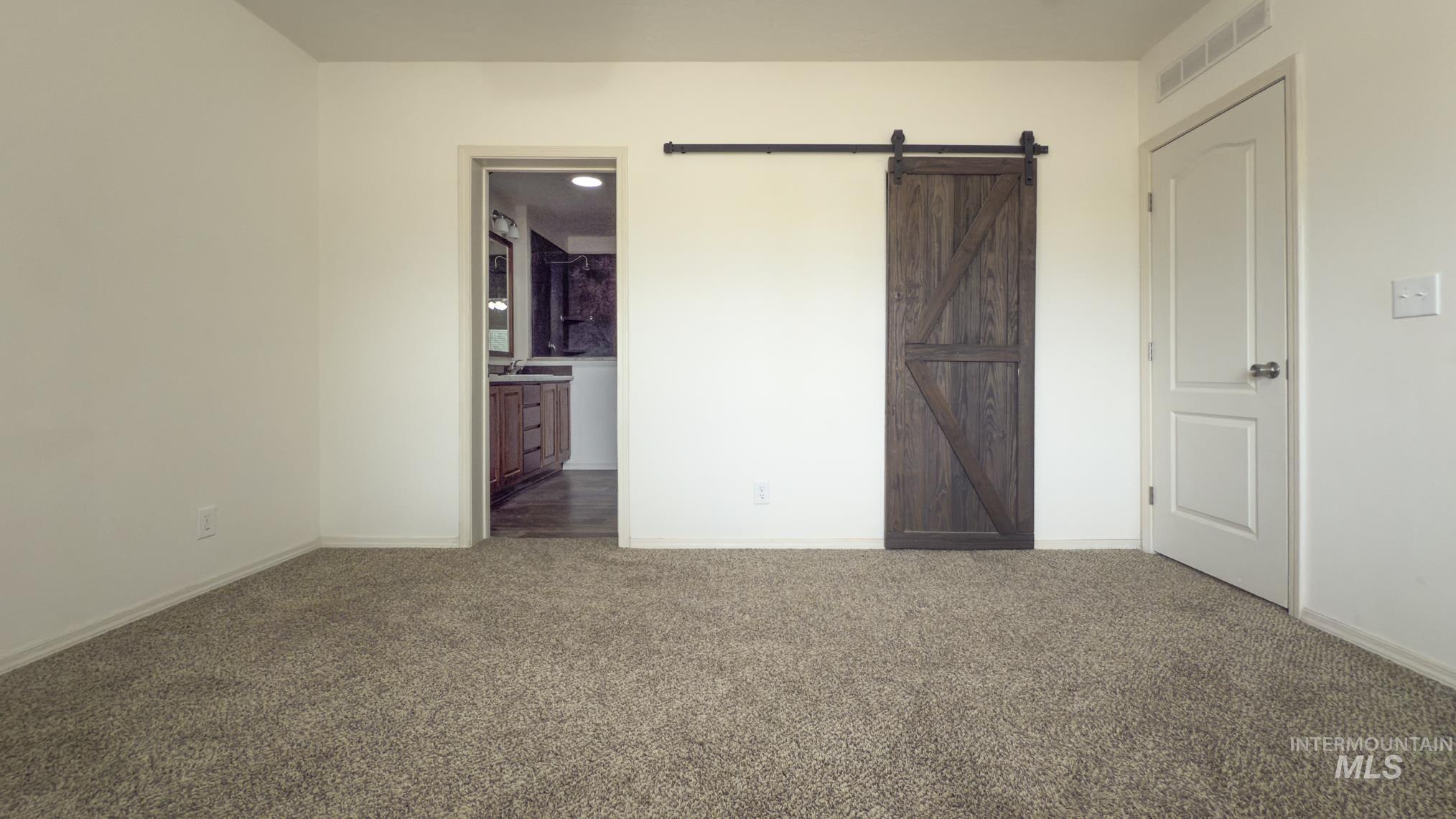 Unfurnished bedroom with a barn door, carpet flooring, and ensuite bathroom
