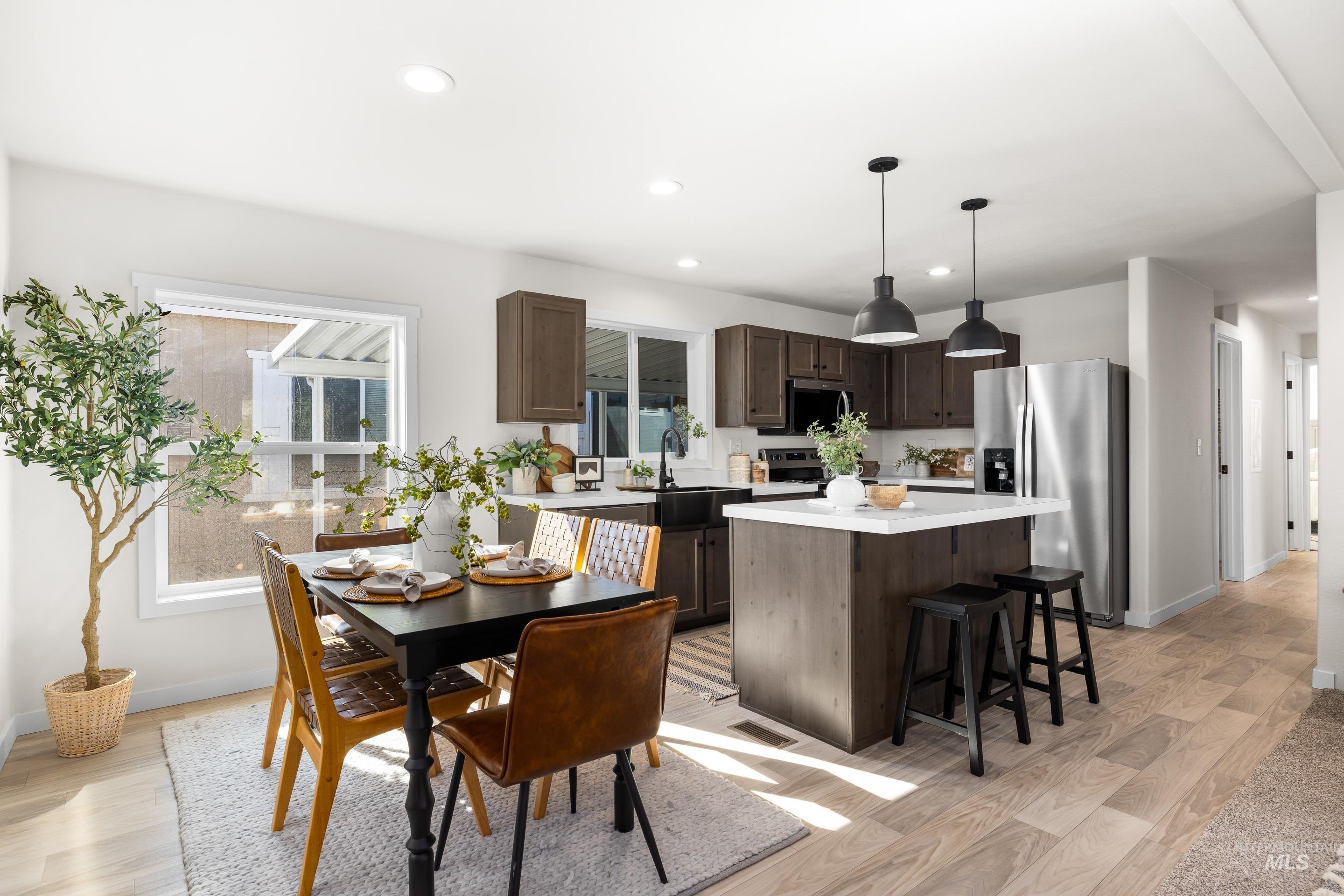 Kitchen with dark brown cabinetry, light countertops, stainless steel appliances, a kitchen island, and pendant lighting