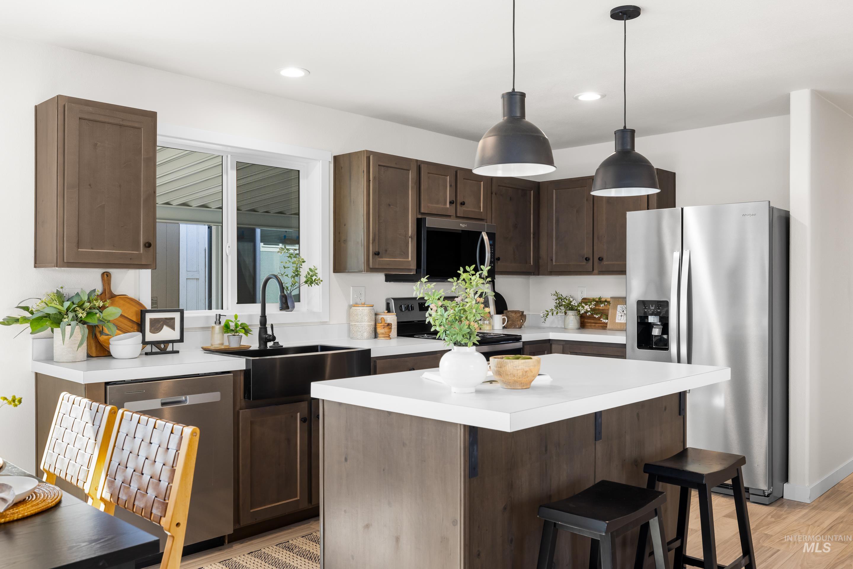 Kitchen with appliances with stainless steel finishes, a breakfast bar, a kitchen island, light countertops, and hanging light fixtures