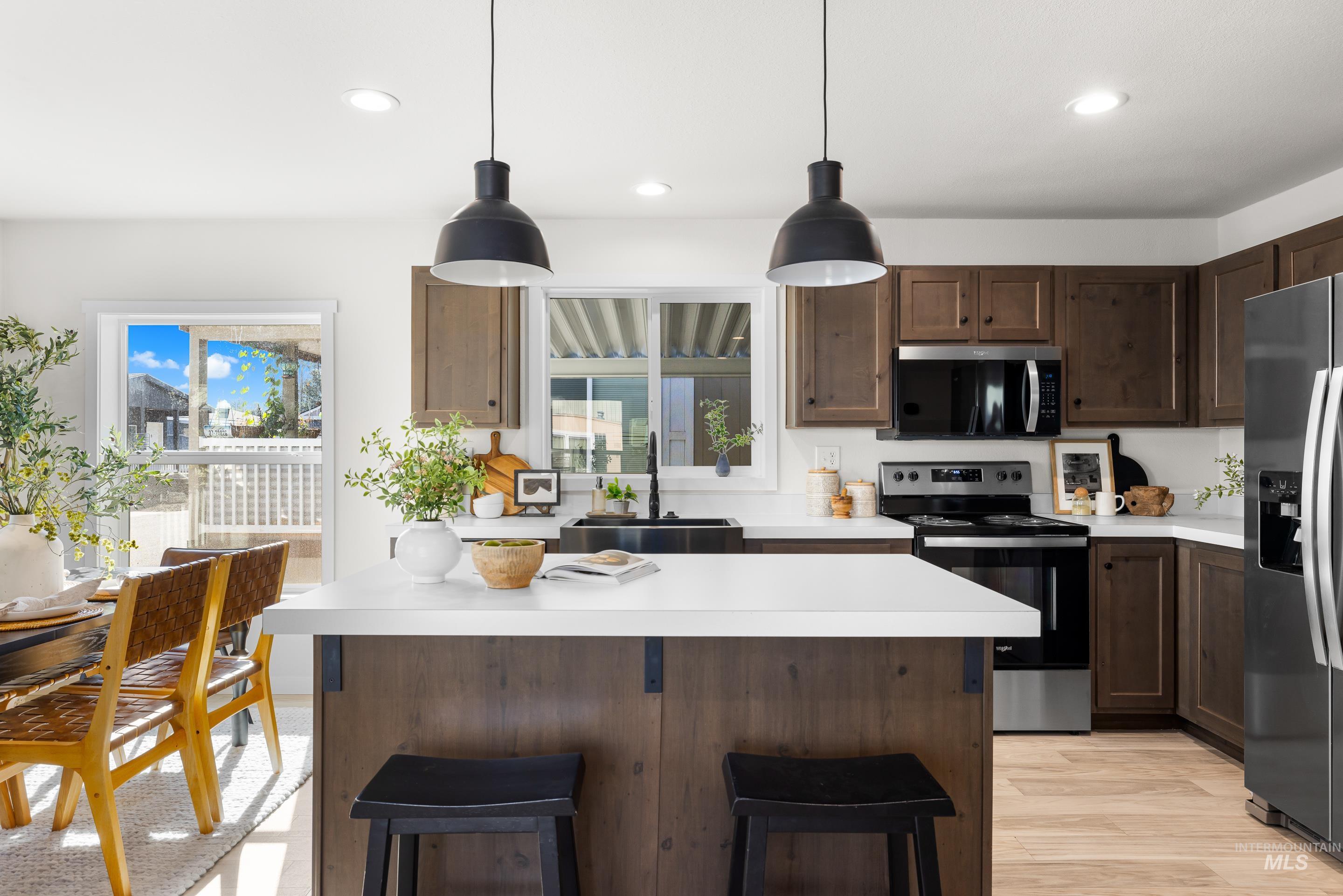 Kitchen with stainless steel appliances, light countertops, pendant lighting, dark brown cabinets, and a breakfast bar area