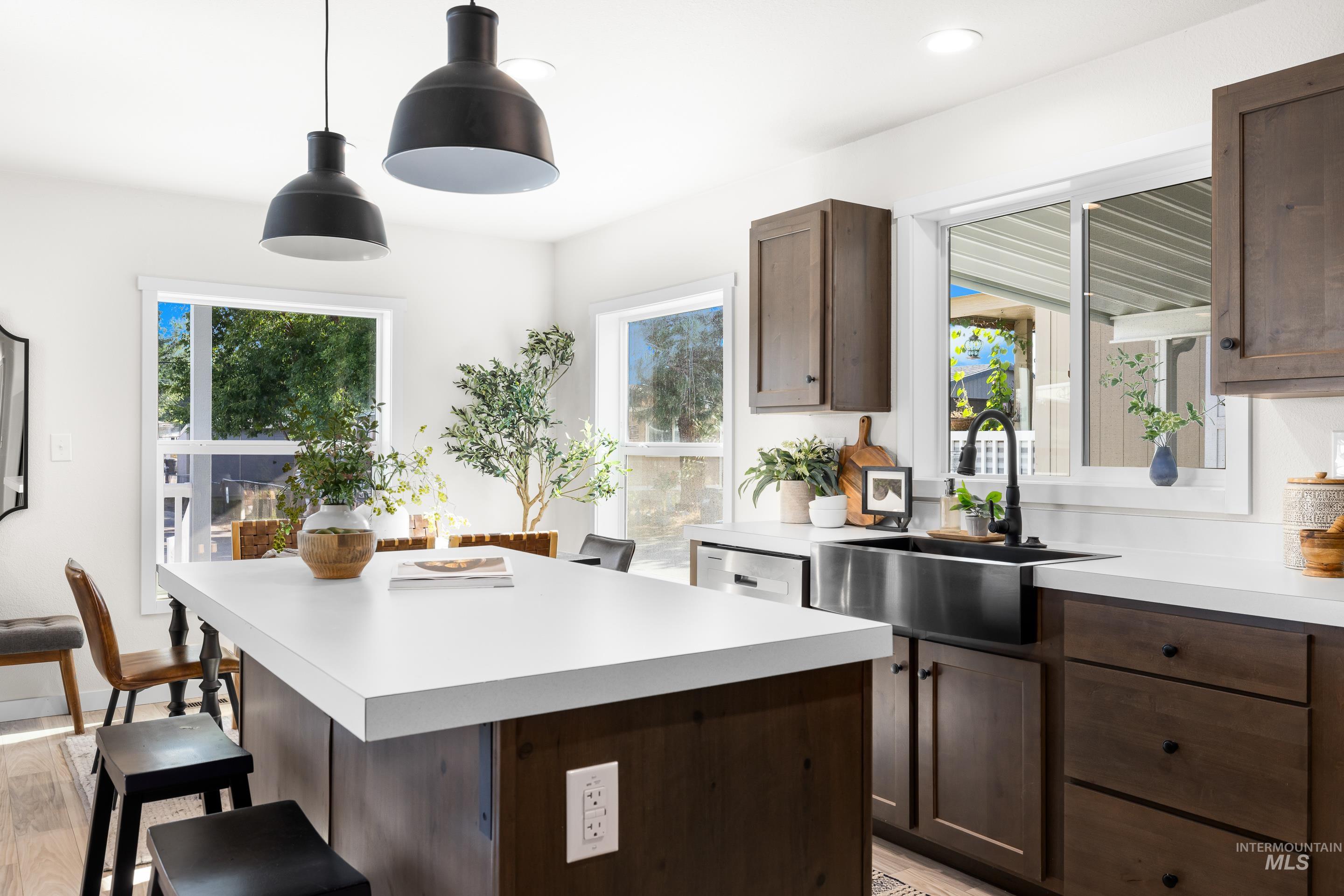 Kitchen with a breakfast bar, light countertops, dark brown cabinetry, hanging light fixtures, and a kitchen island