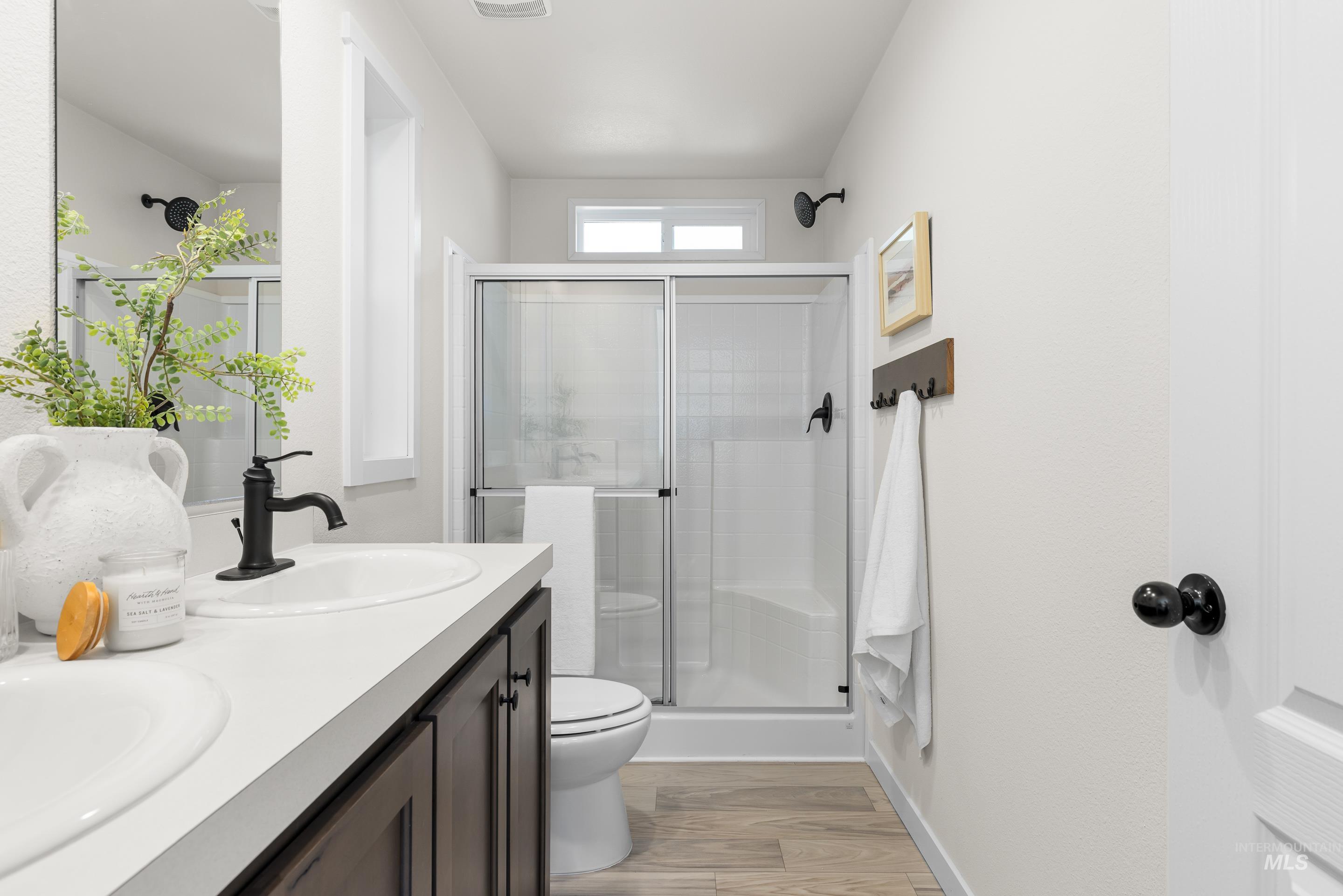 Bathroom with light wood-style floors, a stall shower, and double vanity