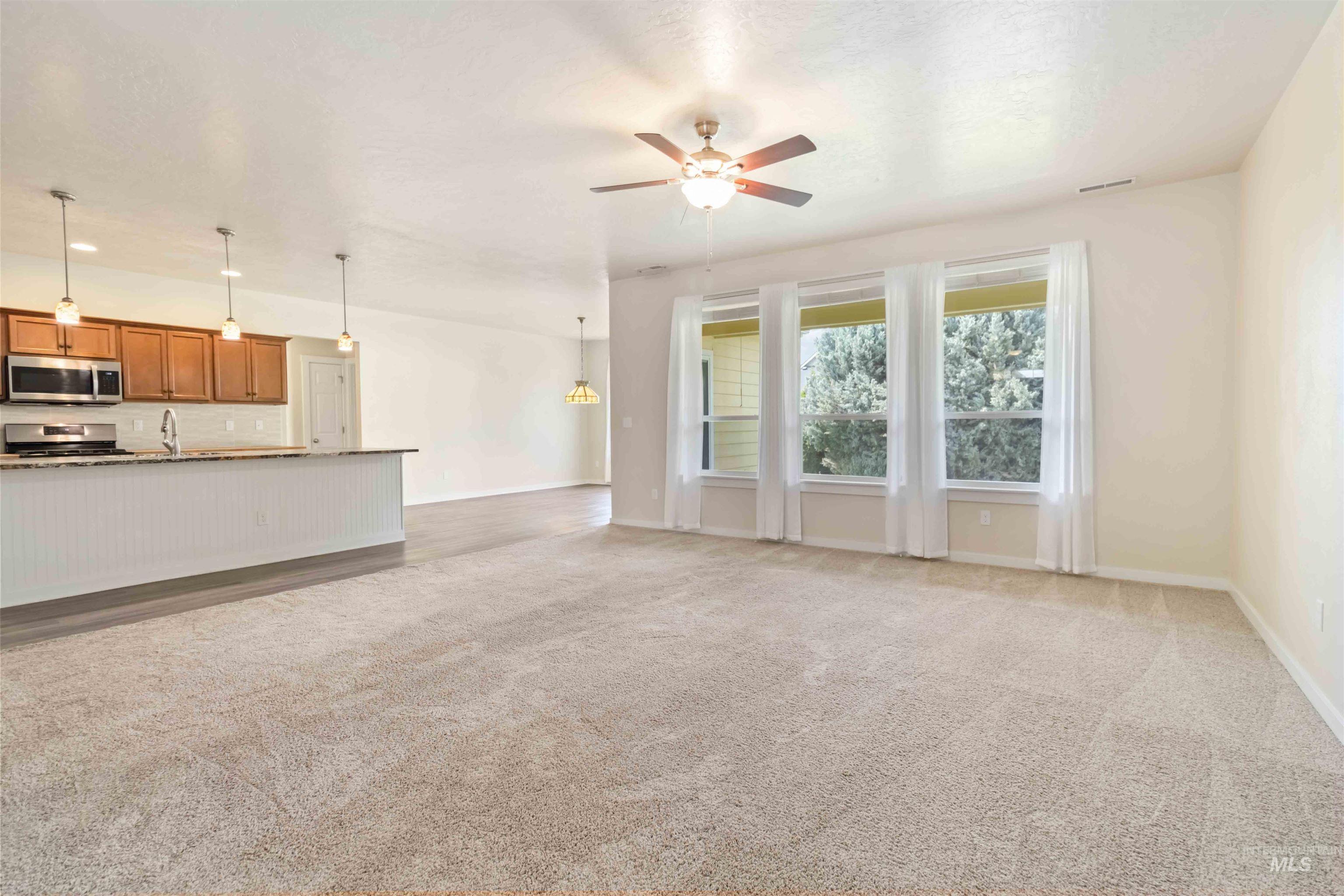 Unfurnished living room with ceiling fan, light carpet, and a chandelier
