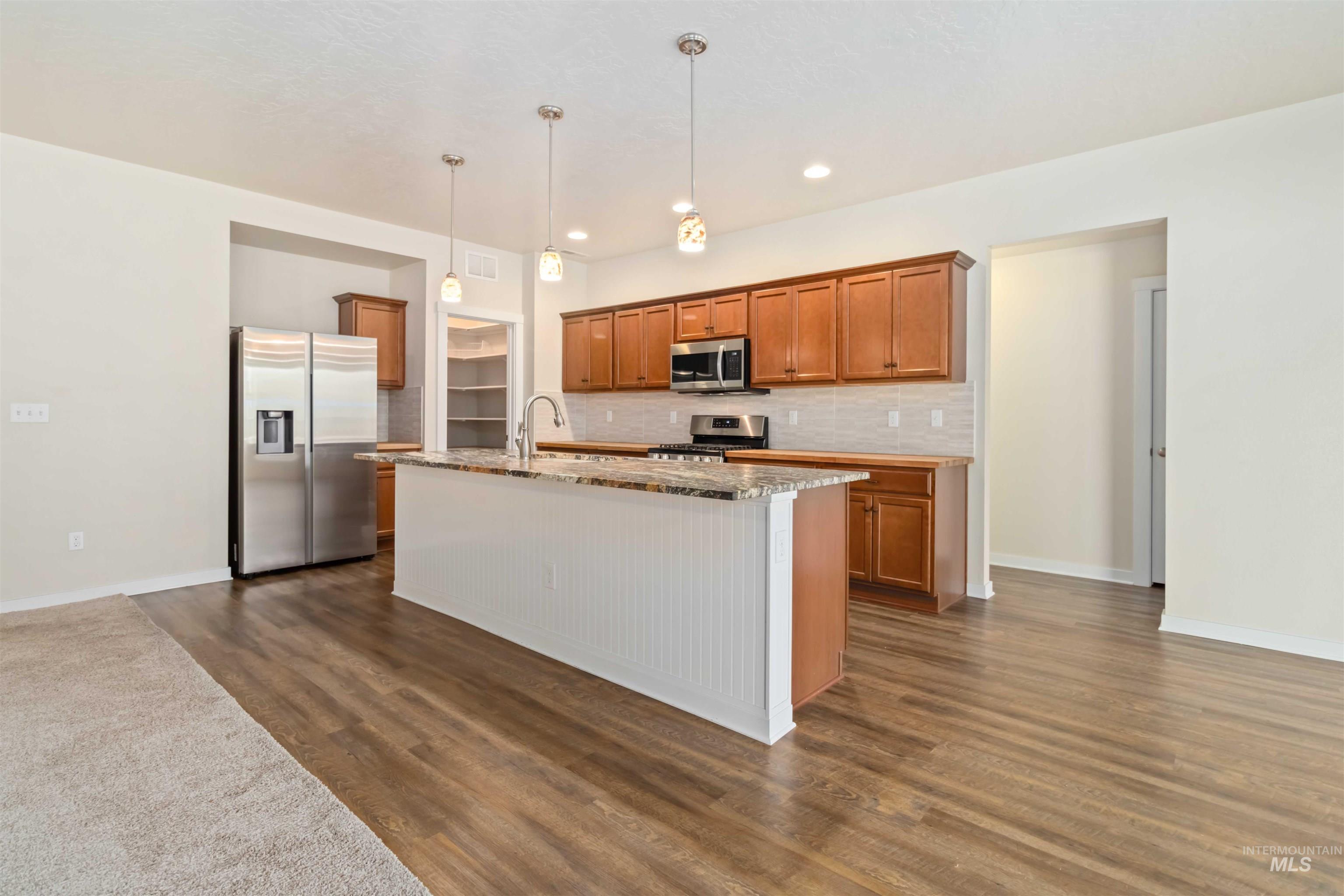 Kitchen featuring brown cabinetry, stainless steel appliances, tasteful backsplash, light stone countertops, and hanging light fixtures