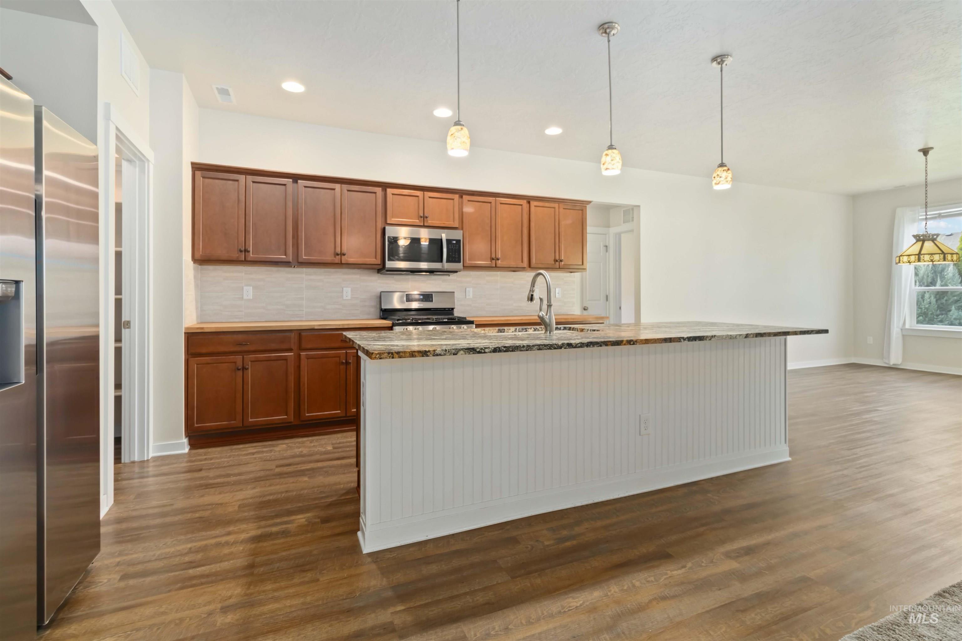 Kitchen featuring brown cabinets, backsplash, stainless steel appliances, light stone countertops, and recessed lighting