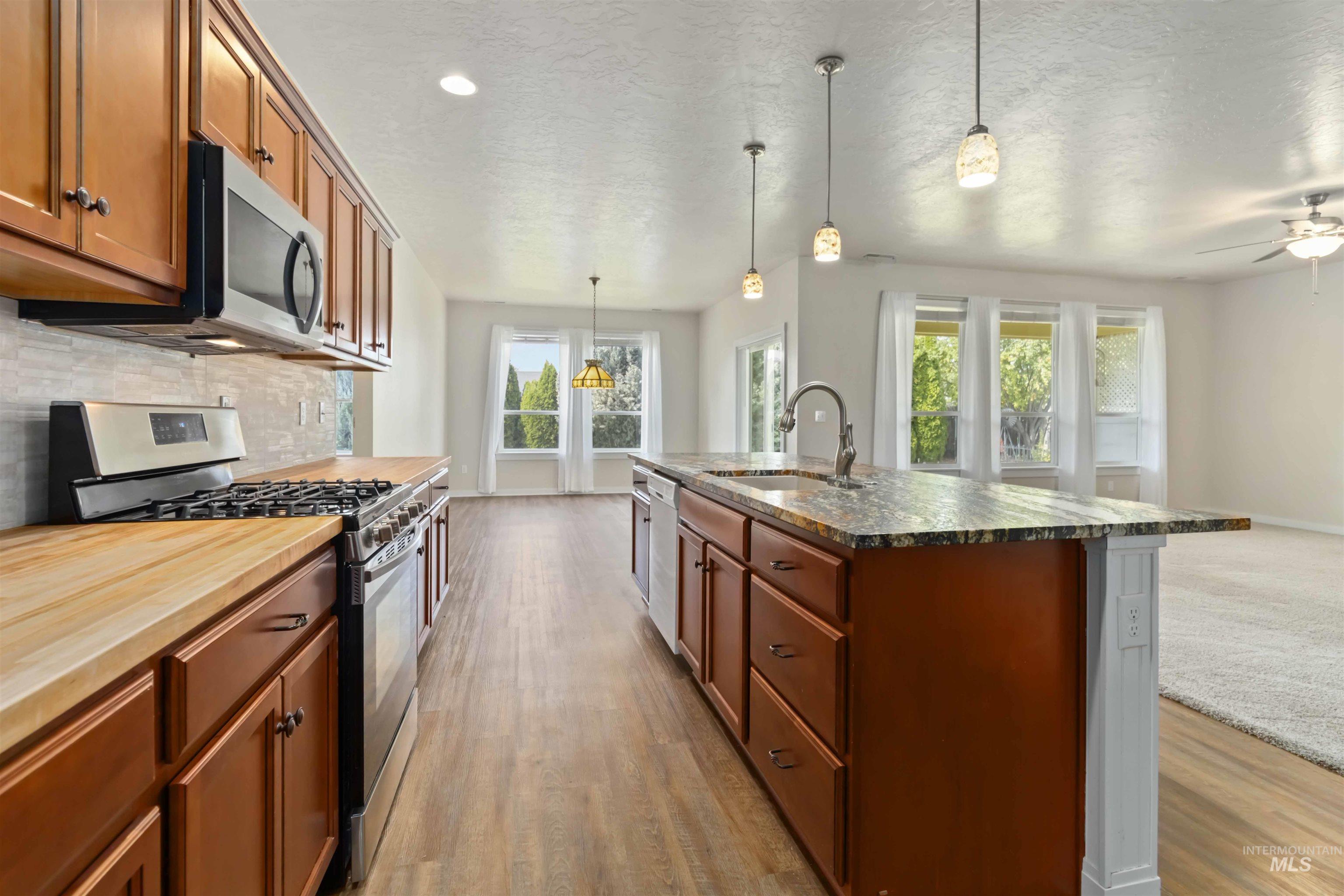 Kitchen featuring stainless steel appliances, brown cabinets, decorative backsplash, pendant lighting, and a textured ceiling