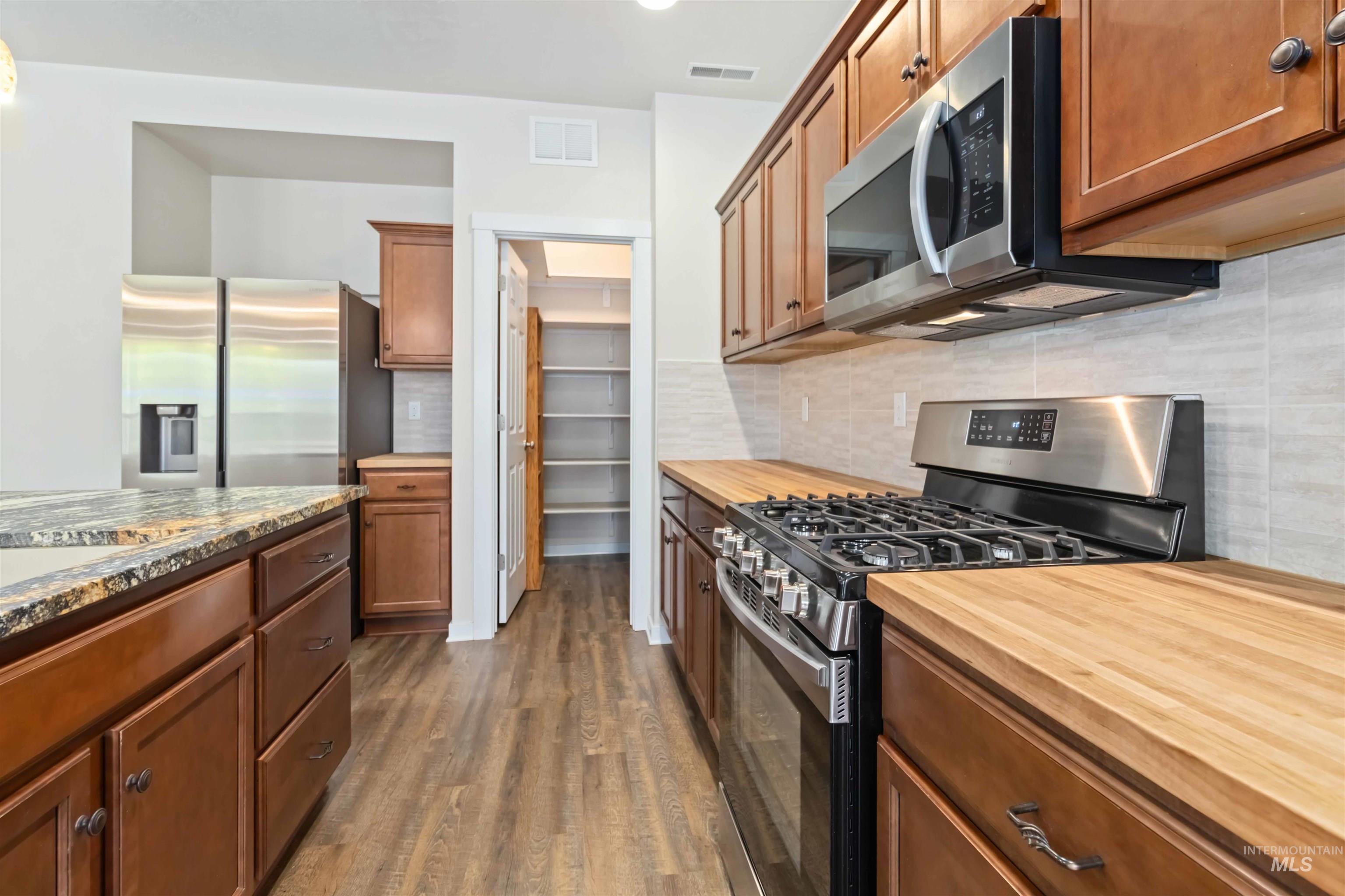 Kitchen with stainless steel appliances, brown cabinetry, tasteful backsplash, dark wood-style floors, and recessed lighting