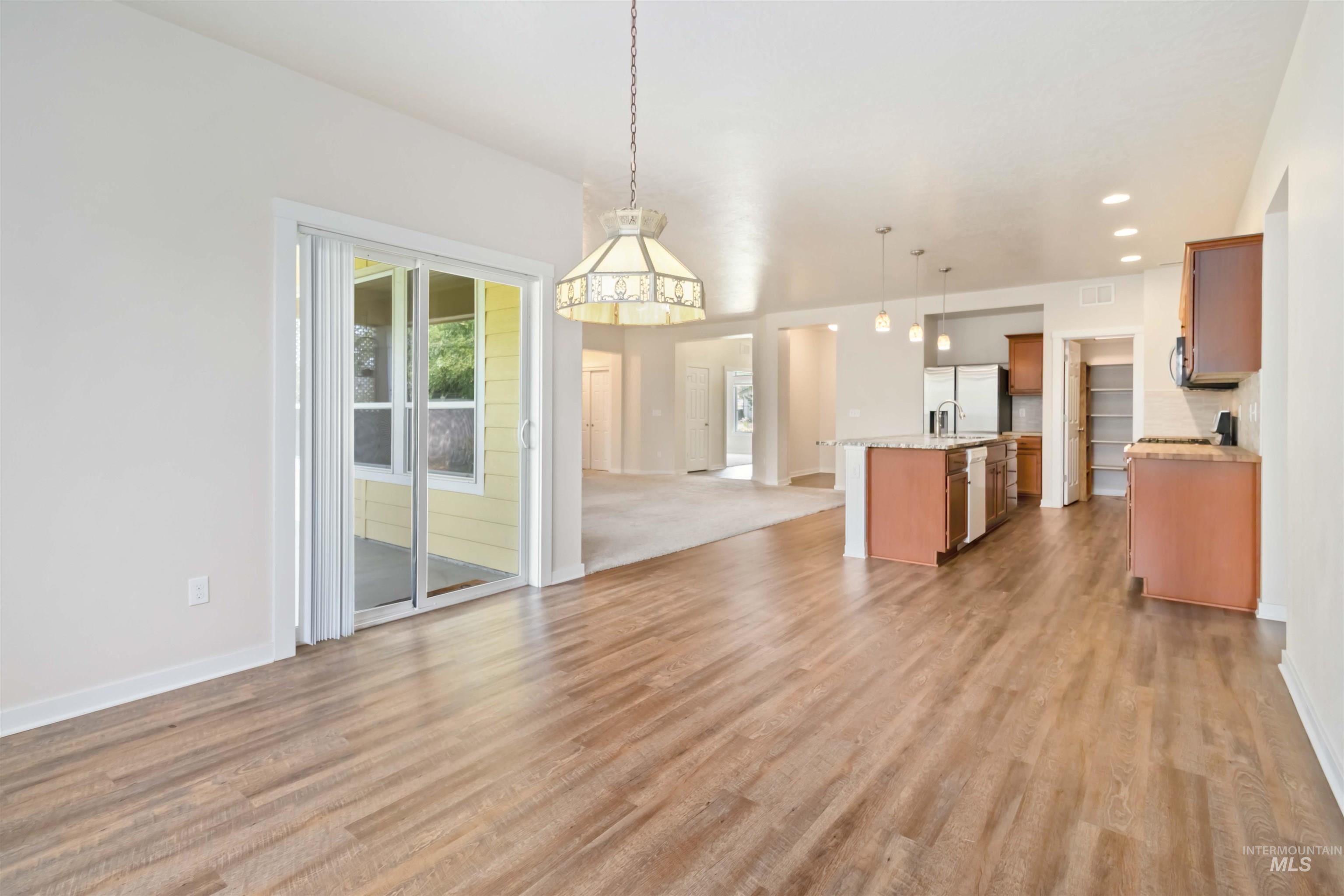 Kitchen featuring open floor plan, a center island with sink, hanging light fixtures, light wood finished floors, and stainless steel fridge