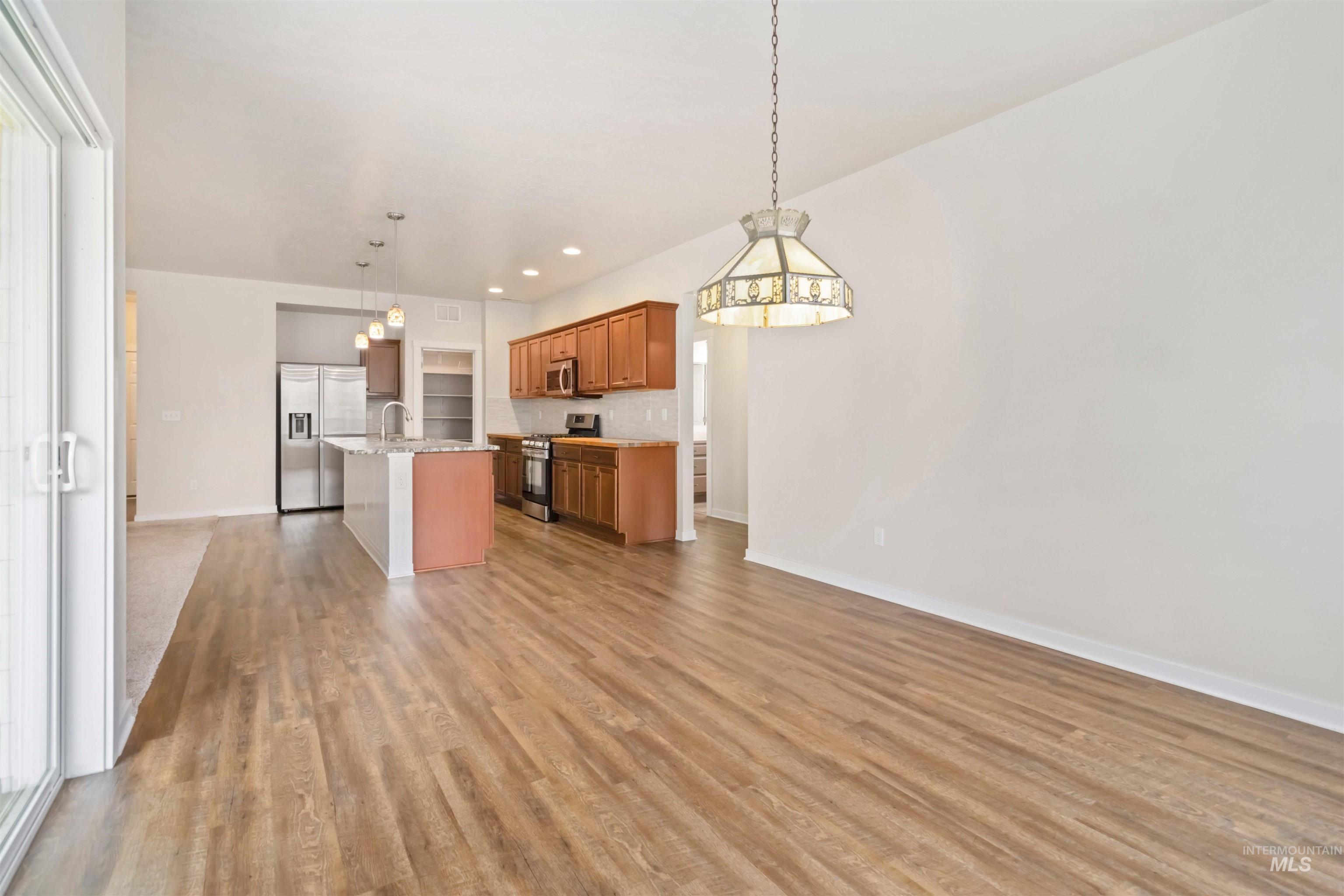 Kitchen featuring open floor plan, appliances with stainless steel finishes, a kitchen island with sink, hanging light fixtures, and recessed lighting