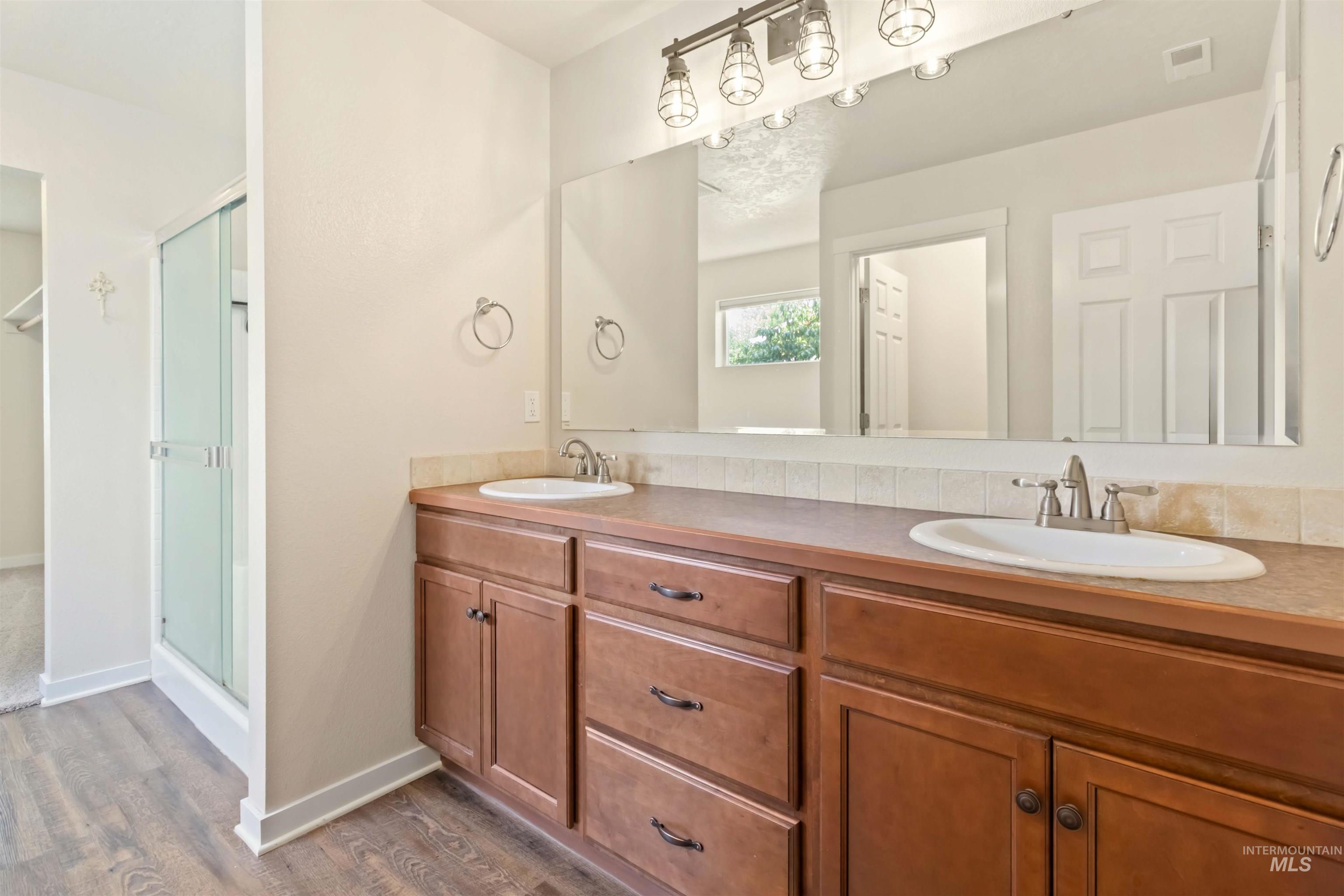 Full bathroom with double vanity, a shower stall, and dark wood finished floors