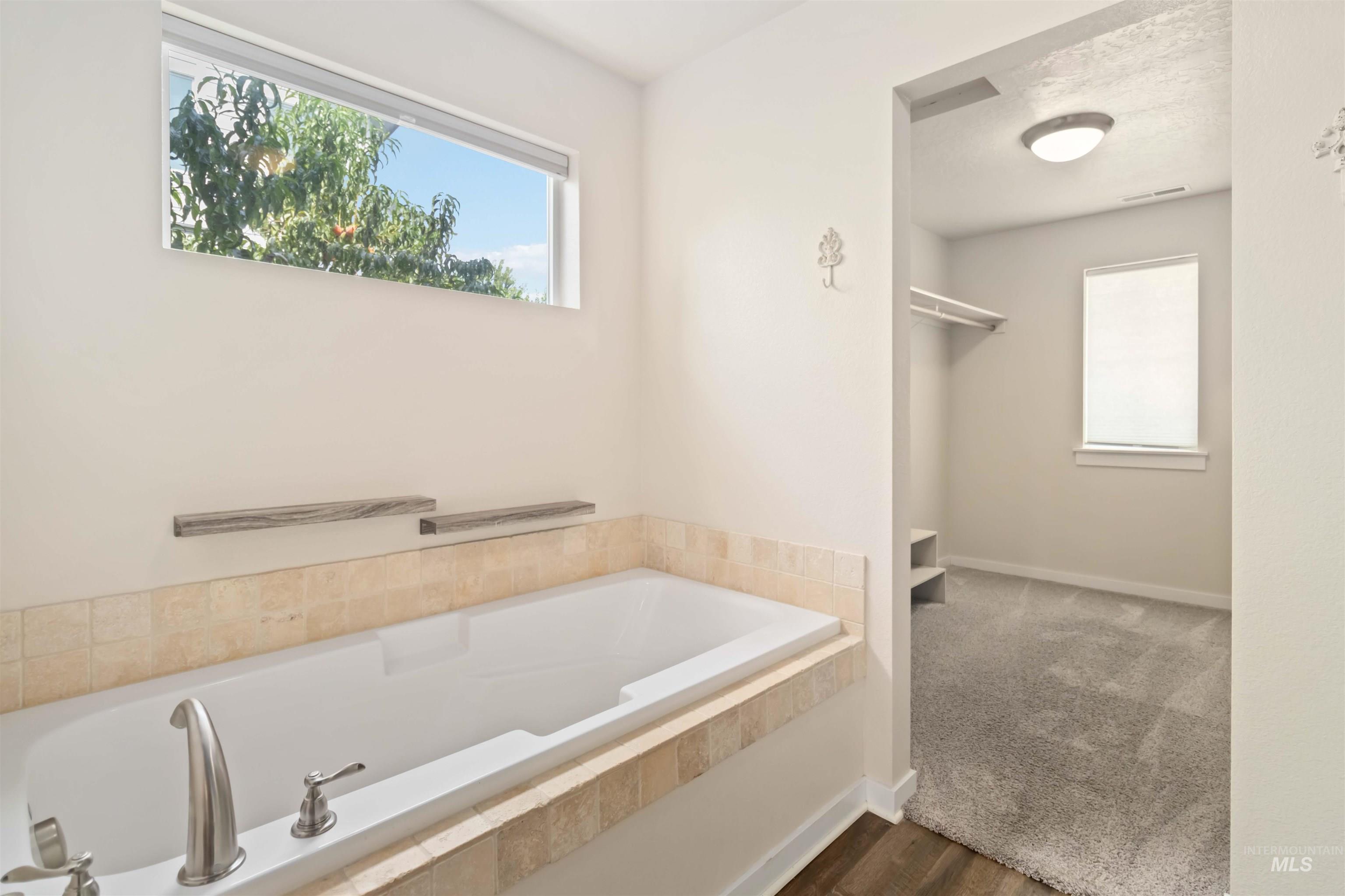 Full bath with a garden tub and dark wood-type flooring
