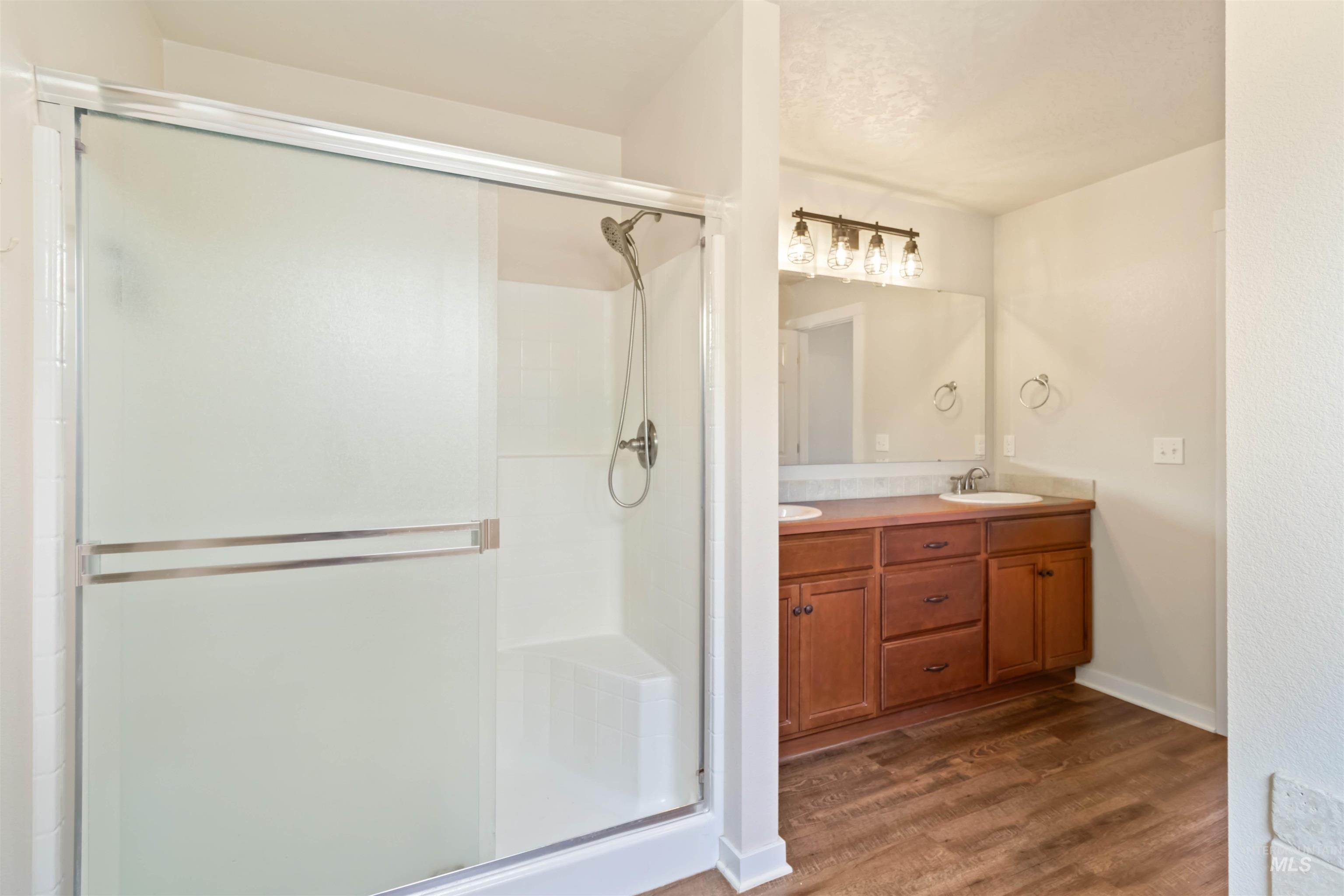 Bathroom with dark wood-style floors, a shower stall, and double vanity