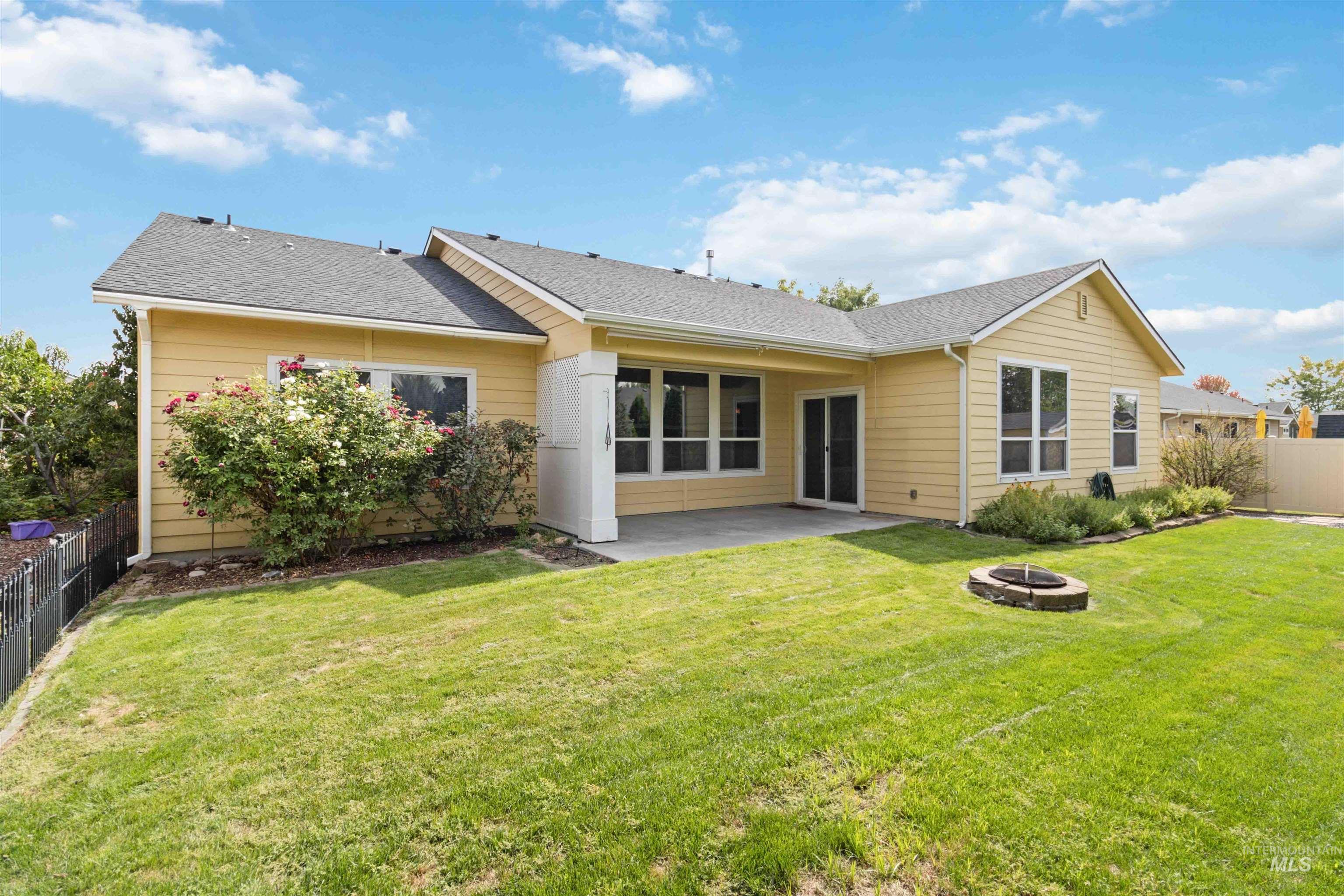 Rear view of house with a shingled roof, a patio area, and an outdoor fire pit