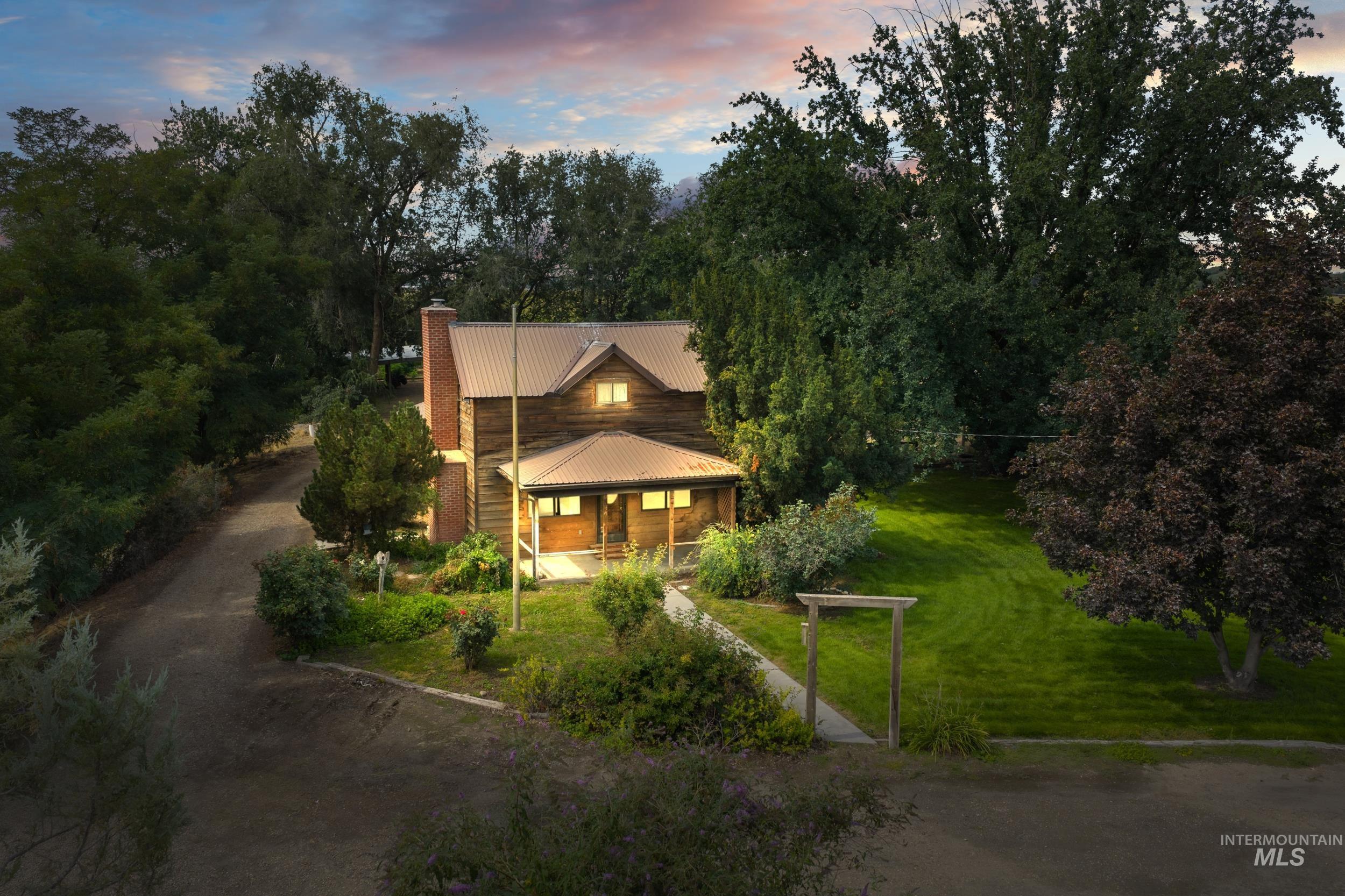 View of front of home featuring a lawn, a porch, a chimney, dirt driveway, and a metal roof