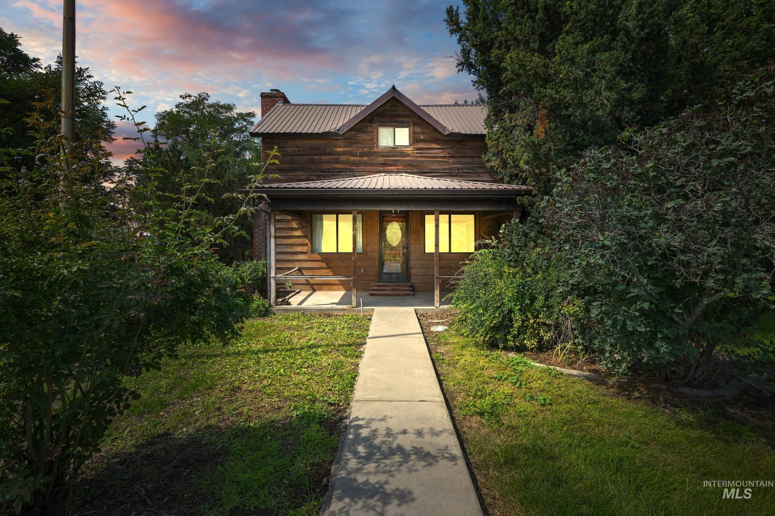 View of front of property featuring a porch, a chimney, a metal roof, and a lawn