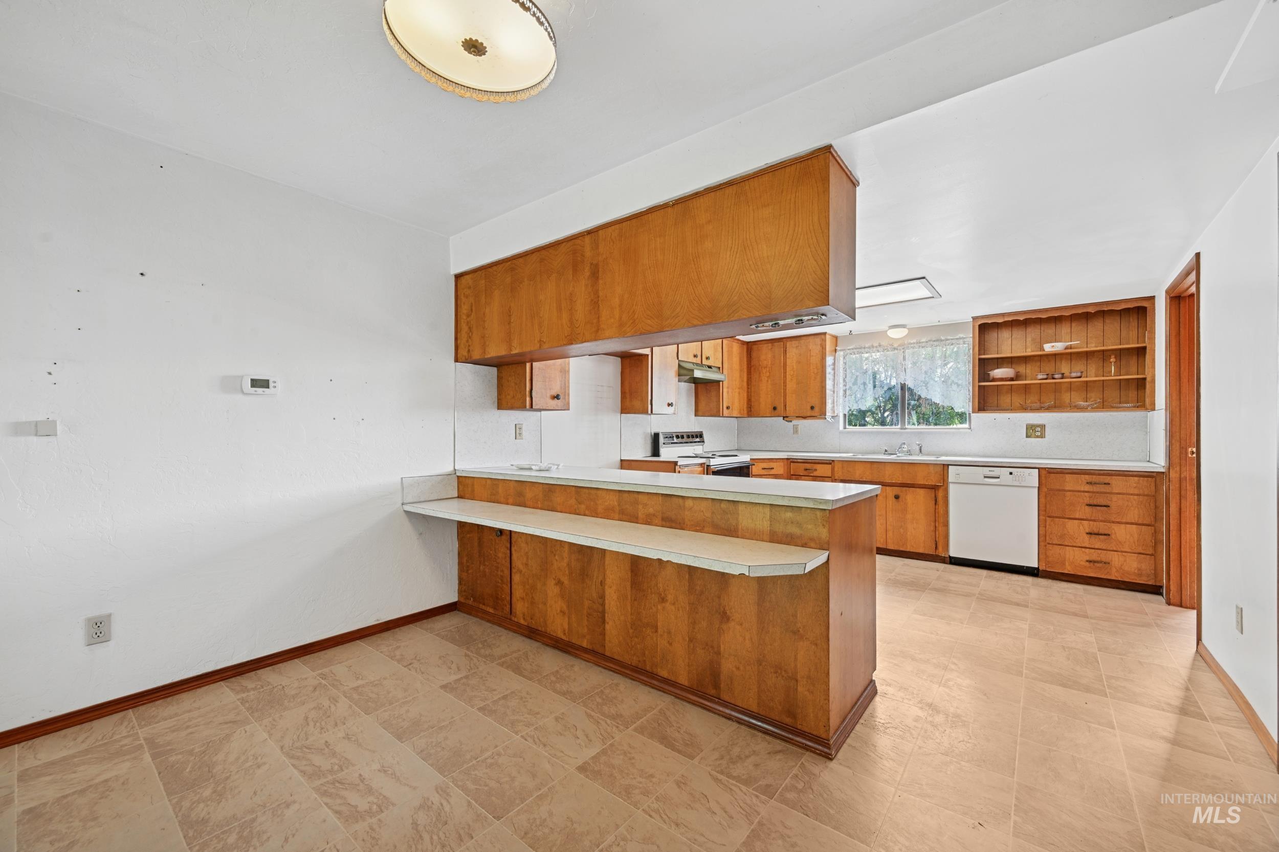 Kitchen featuring brown cabinets, light countertops, a peninsula, white appliances, and a kitchen breakfast bar