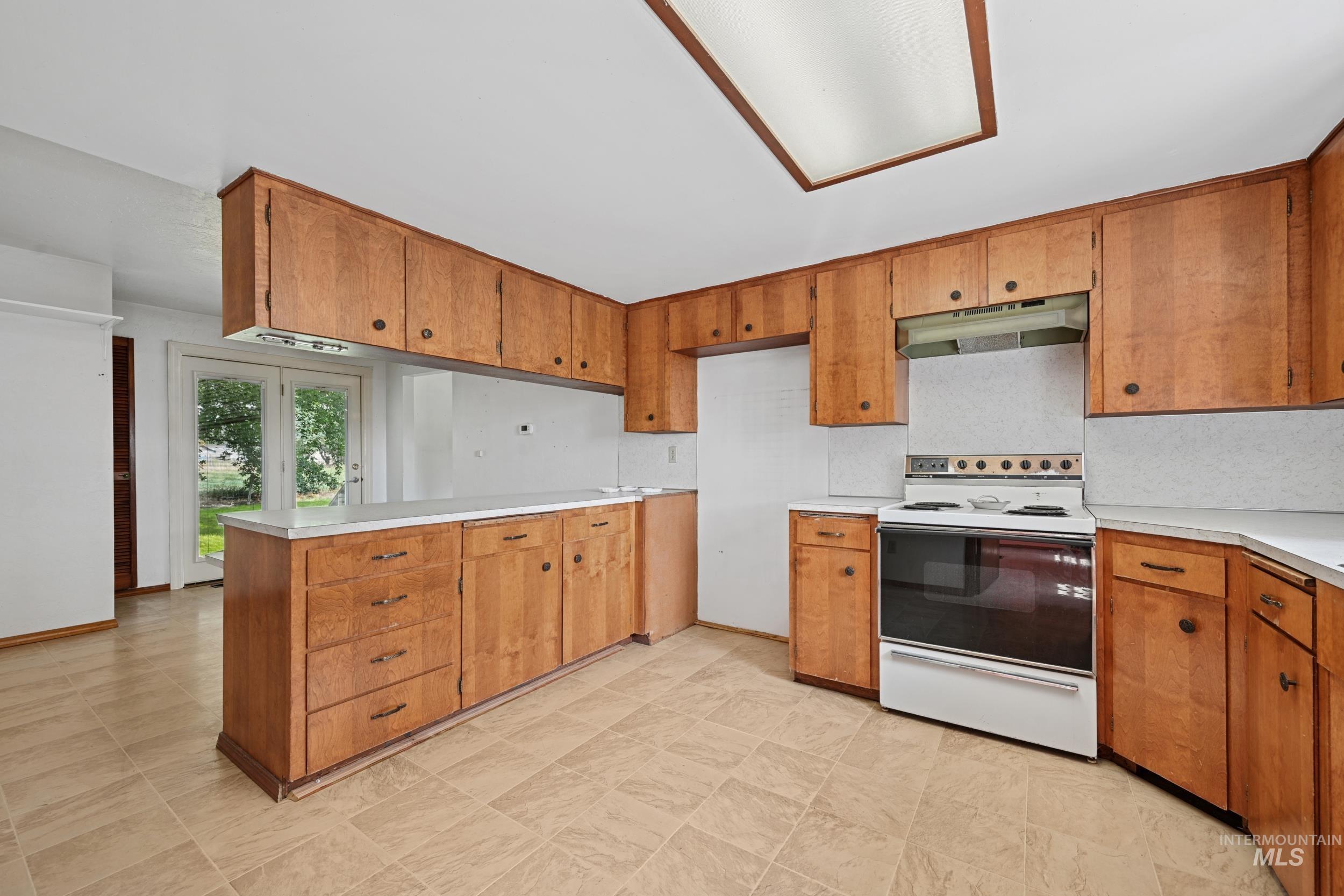 Kitchen with white electric stove, a peninsula, light countertops, and under cabinet range hood