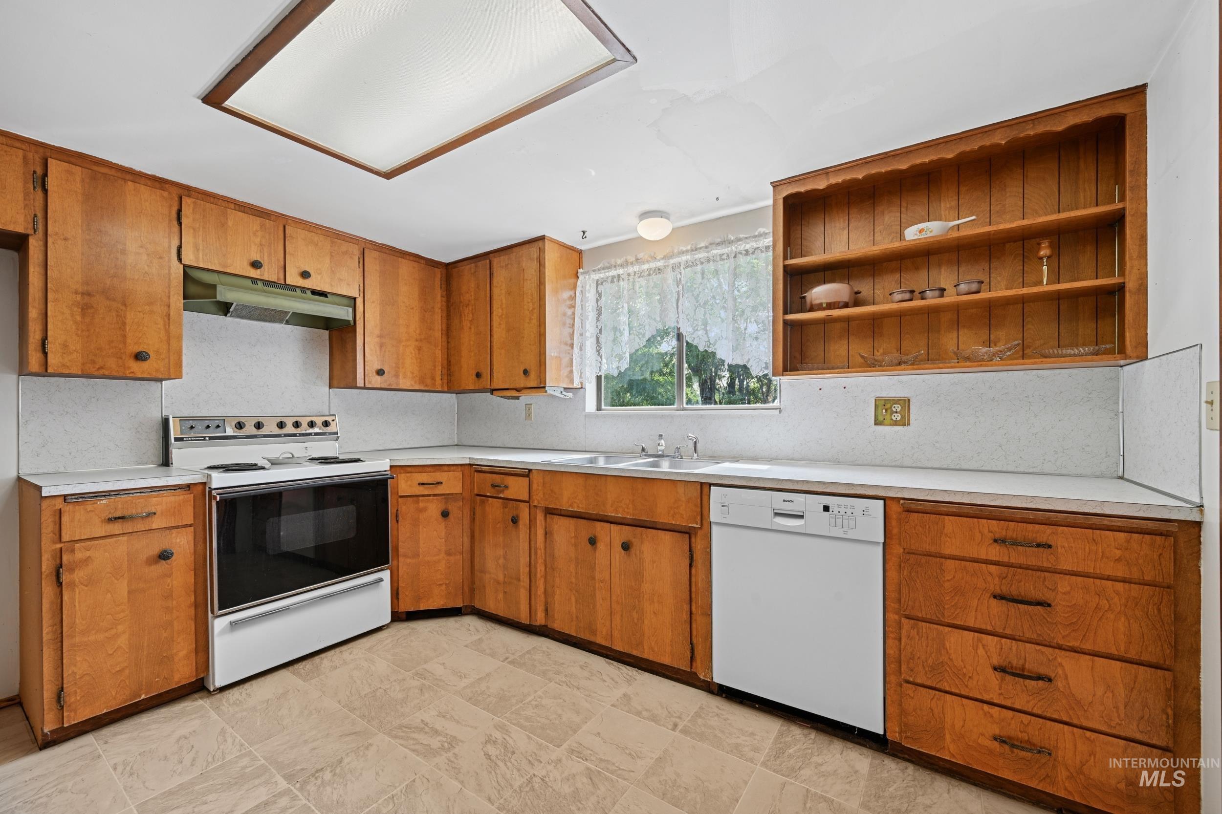 Kitchen with white appliances, light countertops, brown cabinetry, and tasteful backsplash