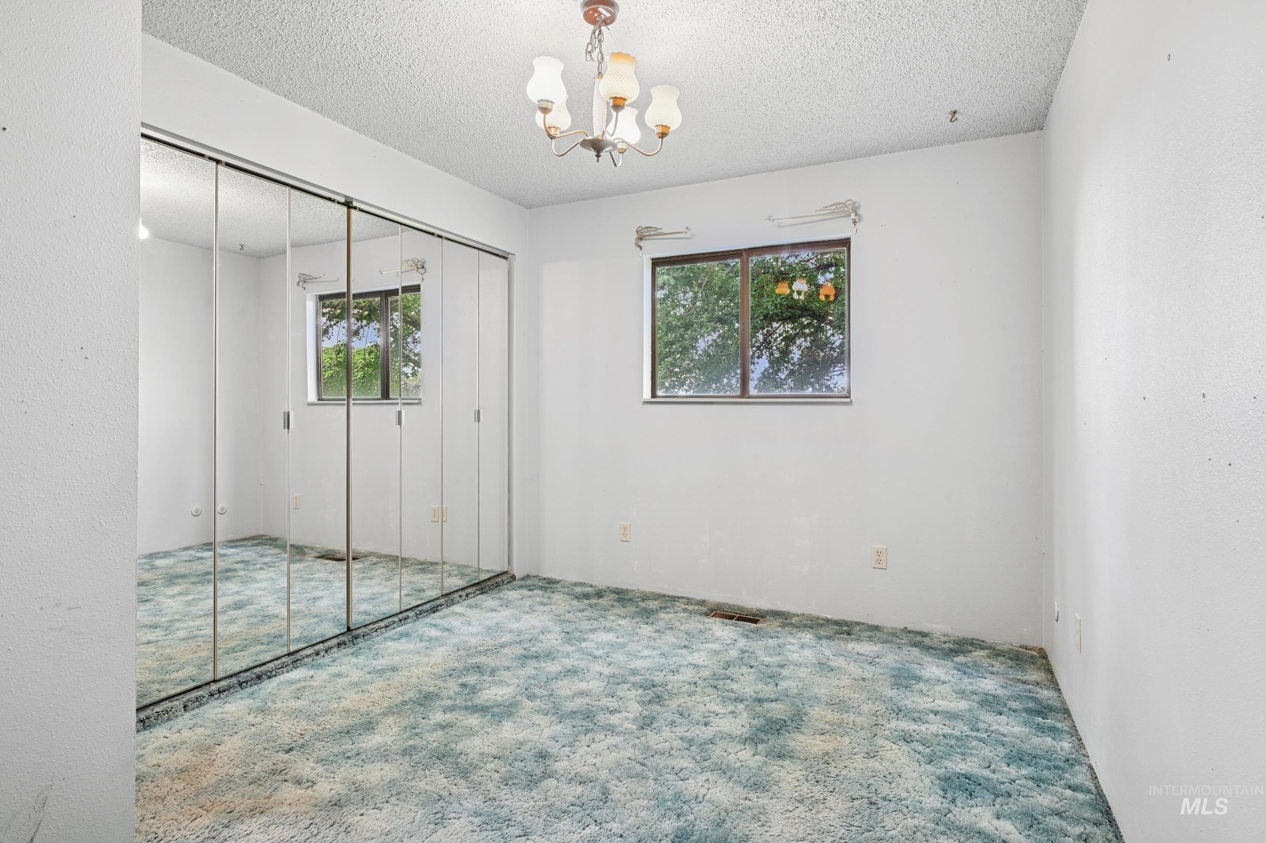 Unfurnished bedroom with carpet flooring, multiple windows, a chandelier, a closet, and a textured ceiling