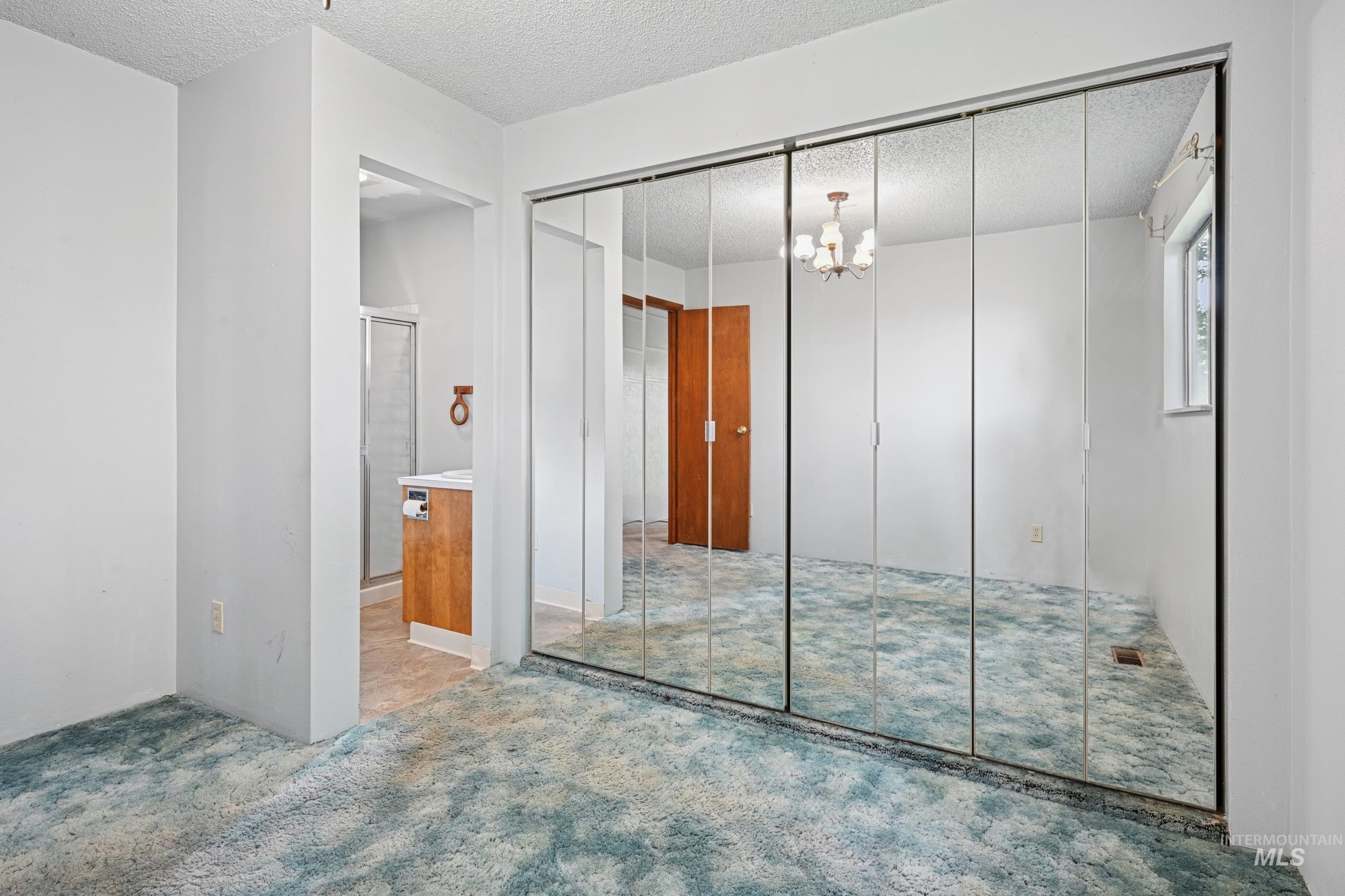 Unfurnished bedroom with a chandelier, a closet, a textured ceiling, carpet, and ensuite bath