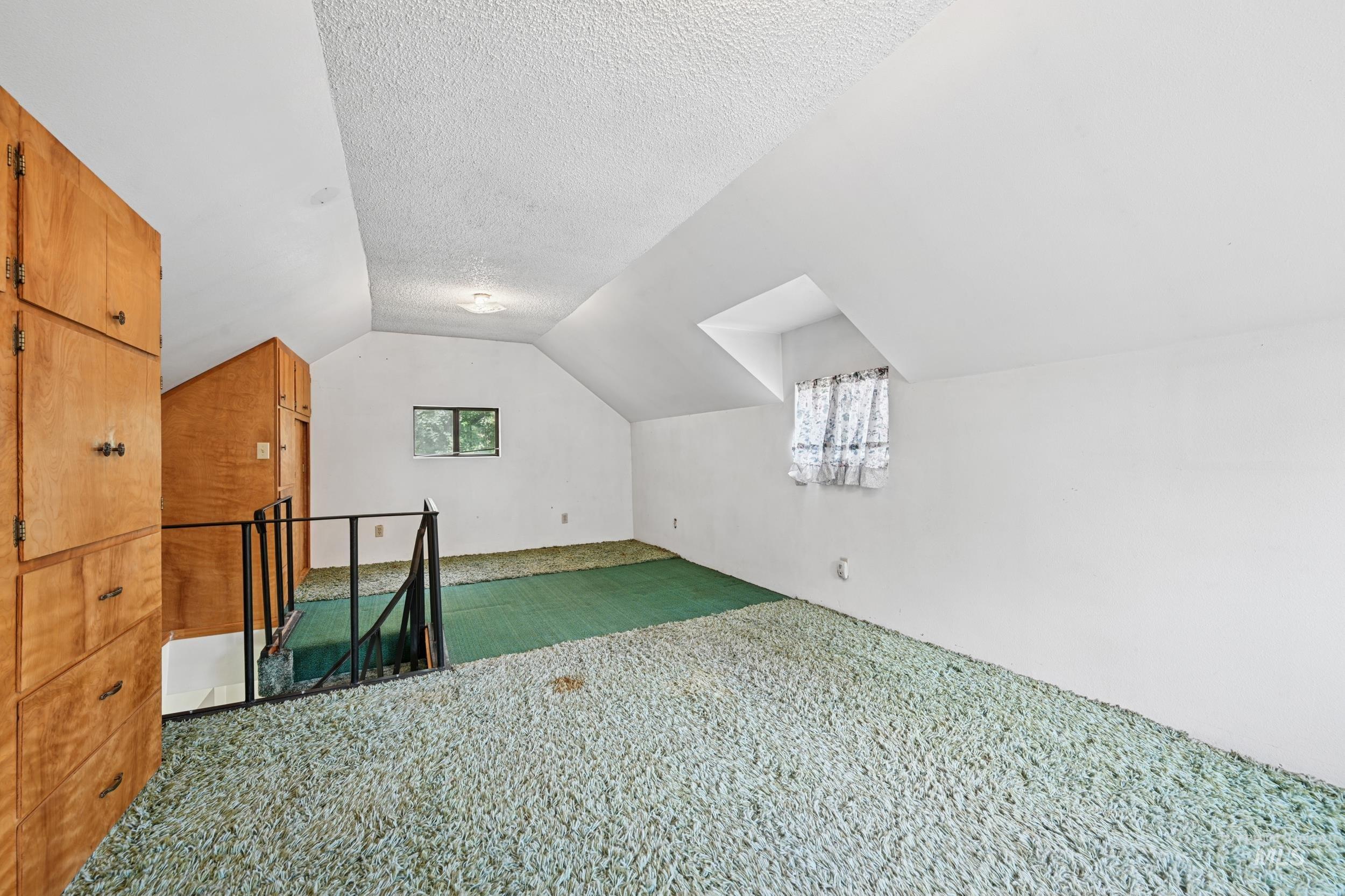 Additional living space featuring vaulted ceiling, carpet floors, and a textured ceiling