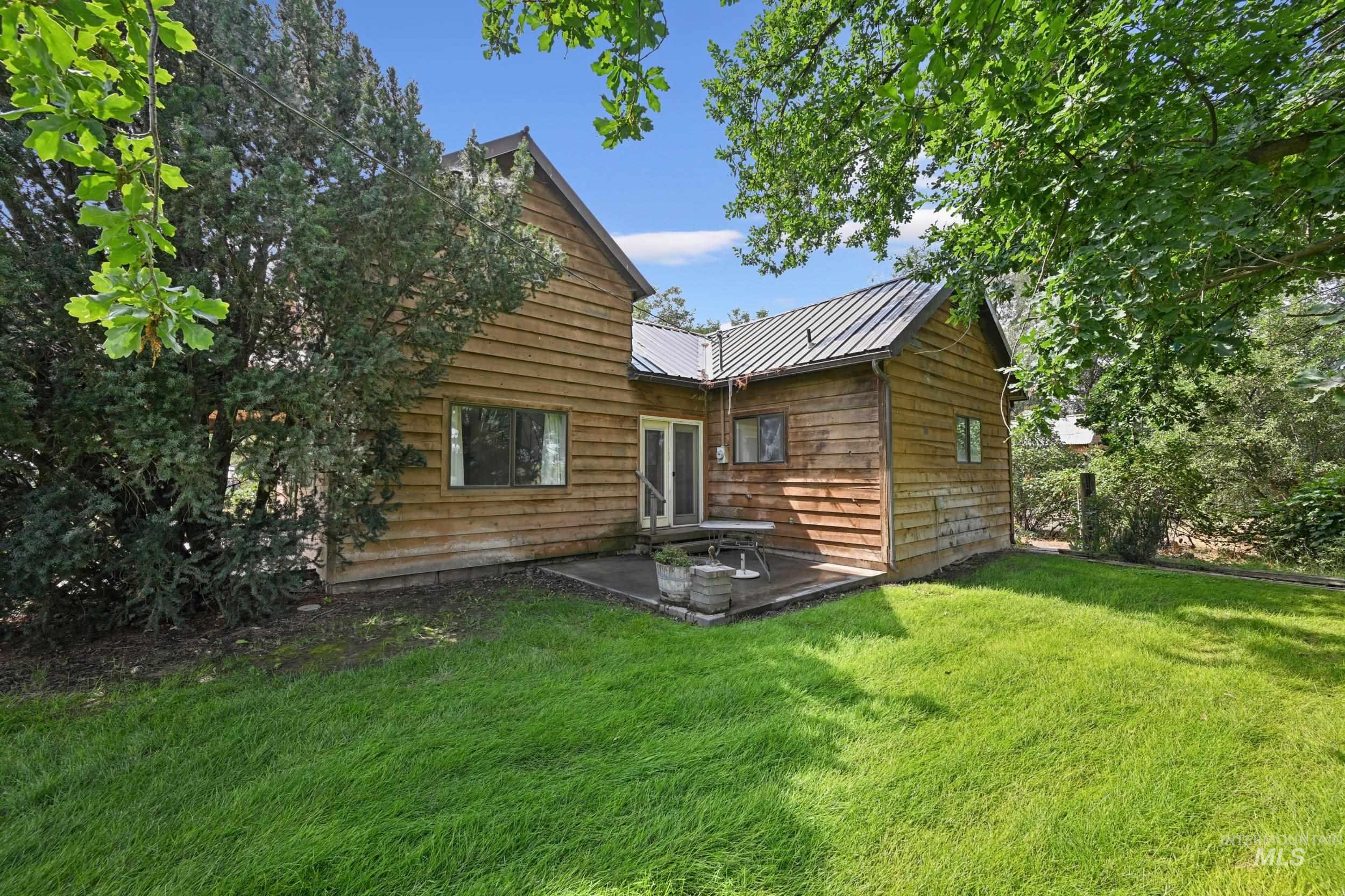 Back of property with a metal roof, a standing seam roof, a lawn, and a patio