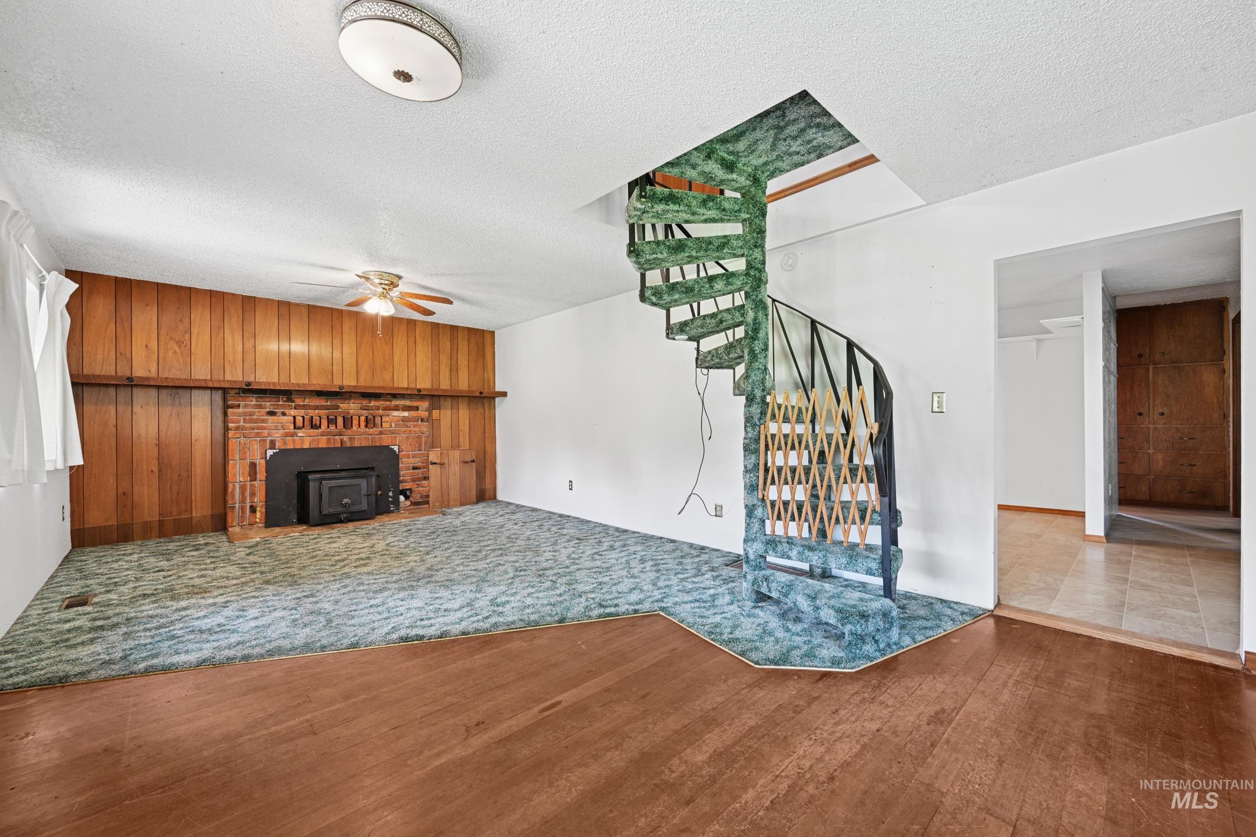 Unfurnished living room featuring a textured ceiling, stairway, wood walls, wood finished floors, and a ceiling fan