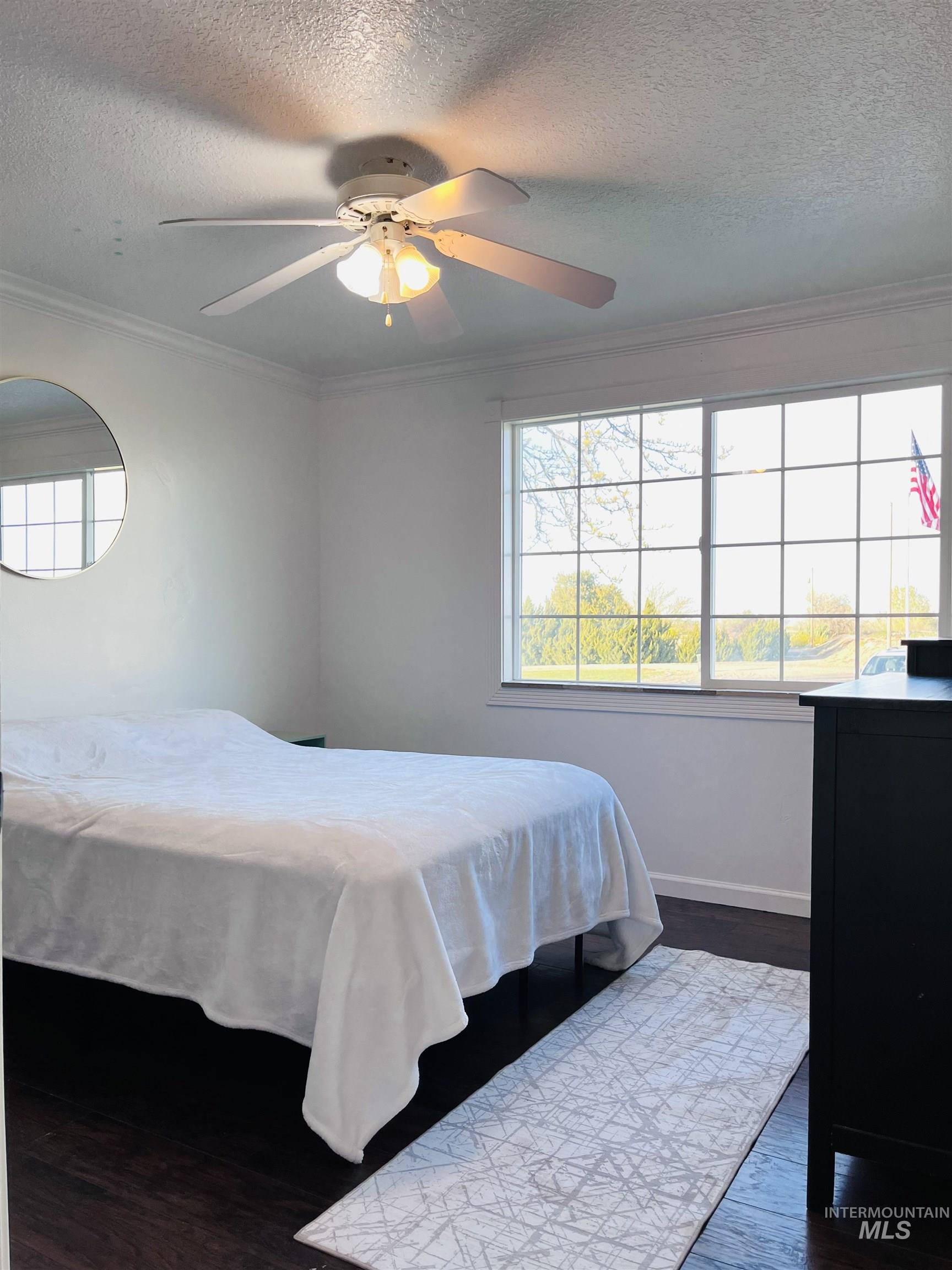 Bedroom with dark wood-type flooring, a textured ceiling, ornamental molding, and ceiling fan