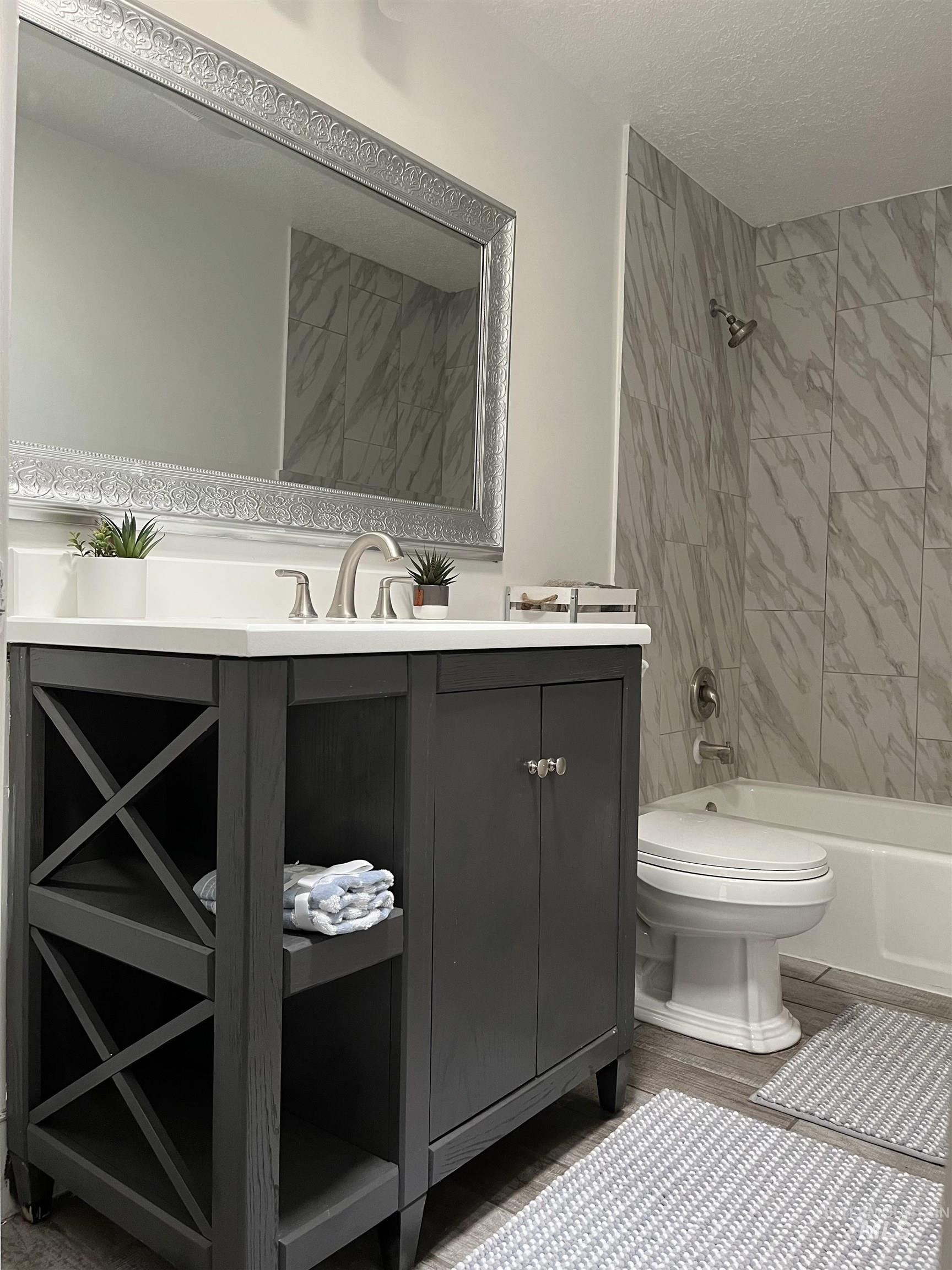 Bathroom with washtub / shower combination, vanity, a textured ceiling, and light wood-style floors