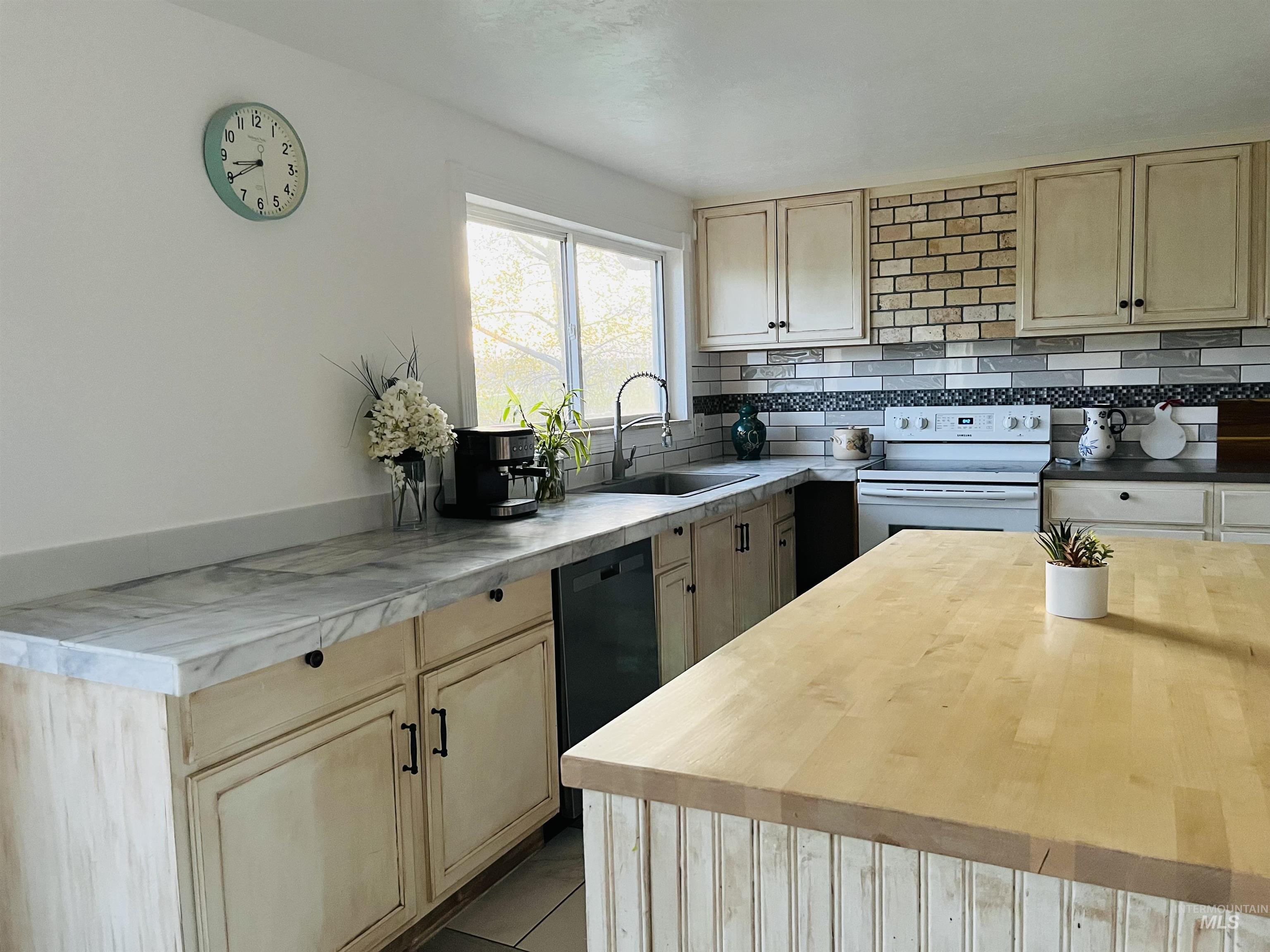 Kitchen with butcher block countertops, light brown cabinets, backsplash, and white range with electric stovetop