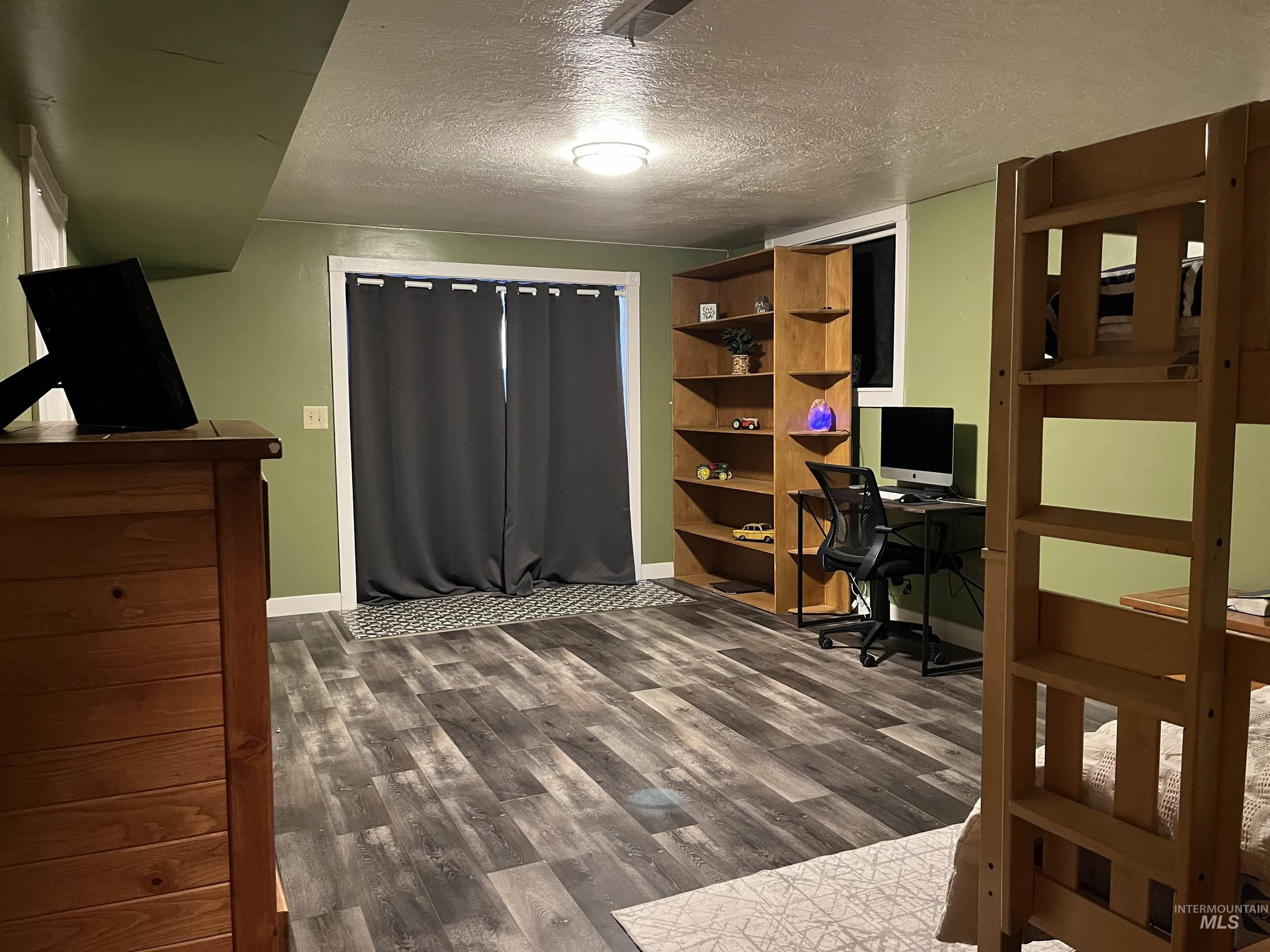 Bedroom with a textured ceiling, a desk, and dark wood-type flooring