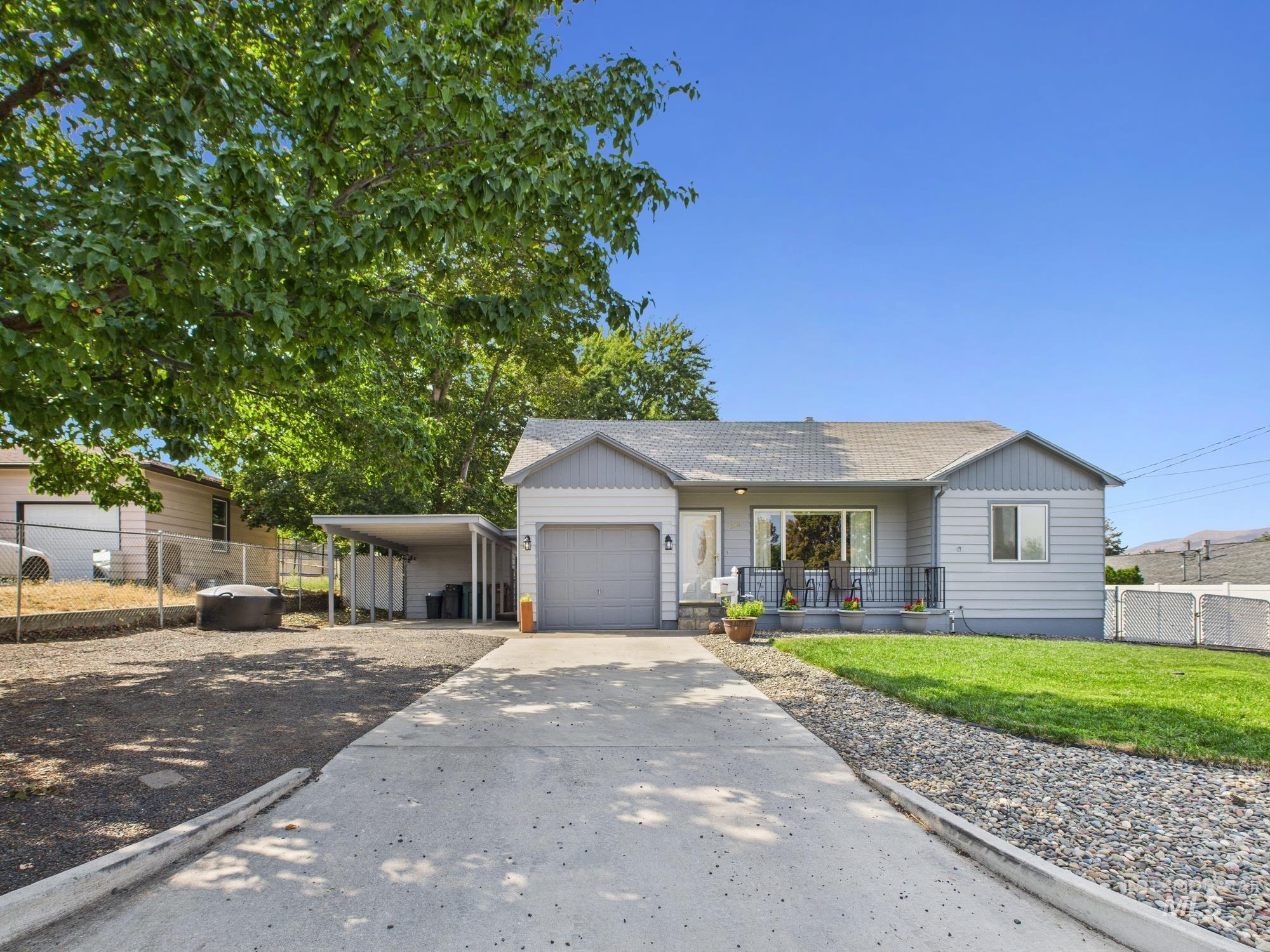 Ranch-style home featuring an attached garage, concrete driveway, a carport, covered porch, and roof with shingles
