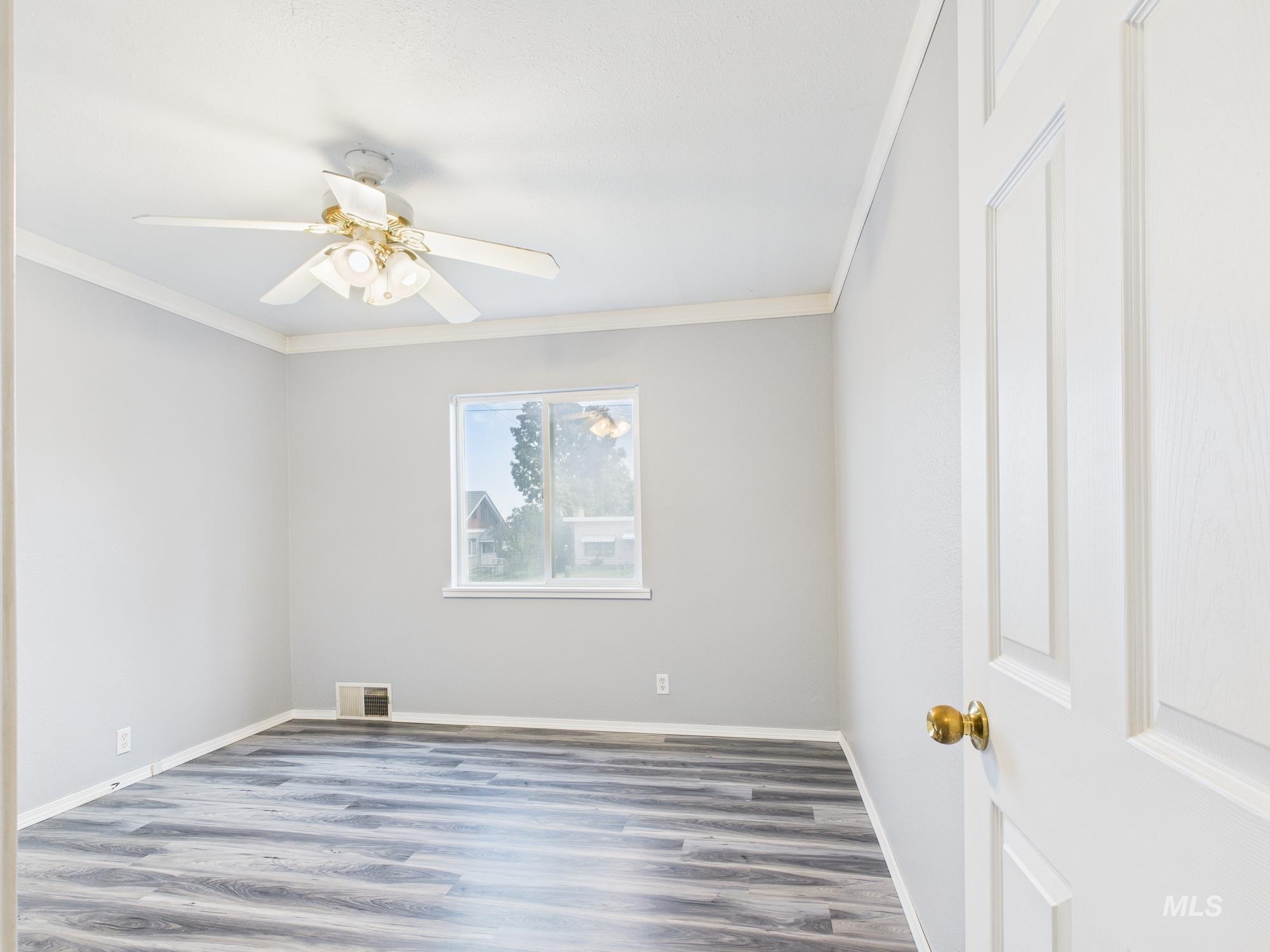 Empty room featuring ornamental molding, wood finished floors, and a ceiling fan