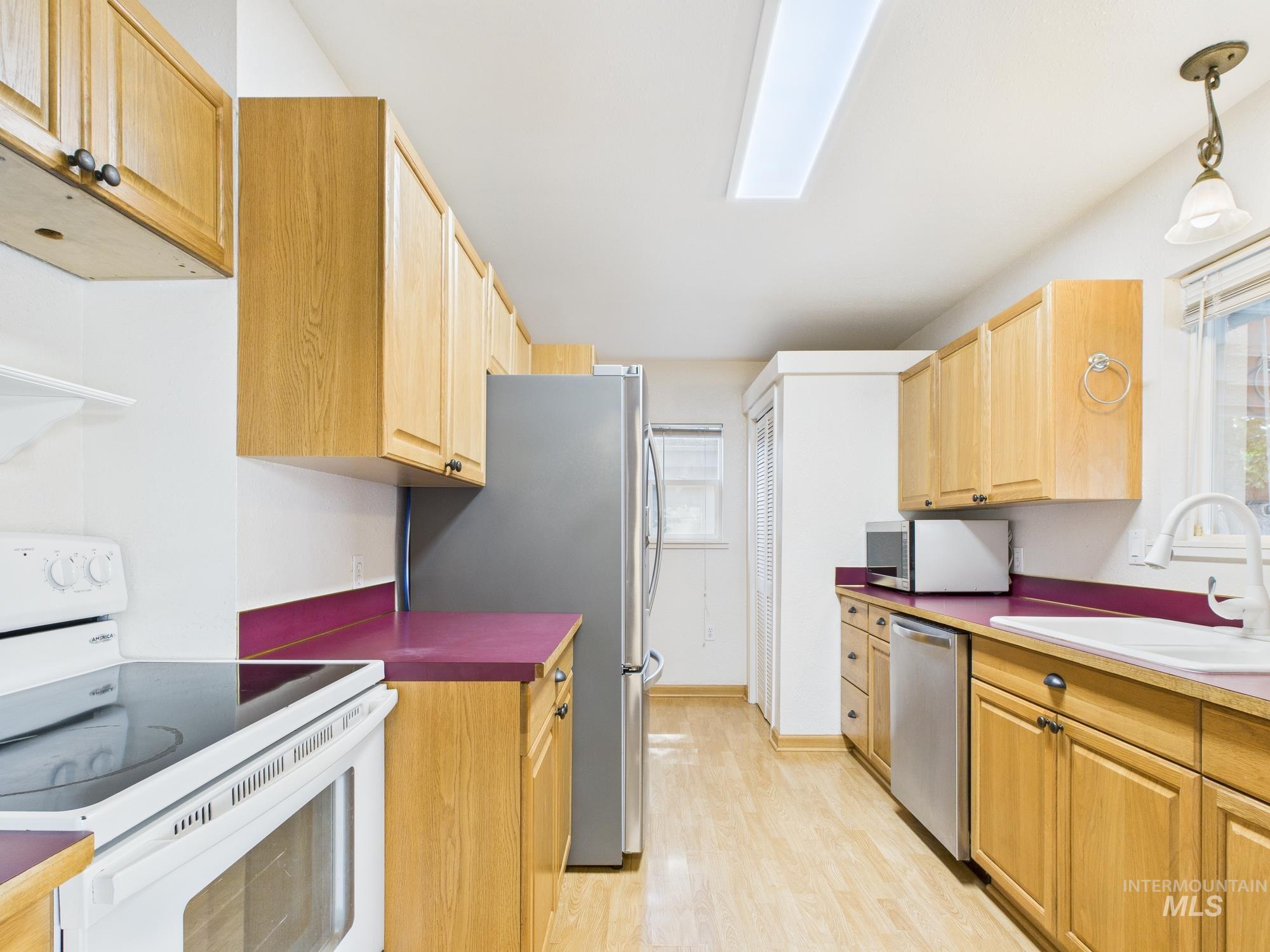 Kitchen featuring appliances with stainless steel finishes, light brown cabinetry, hanging light fixtures, and light wood-style flooring