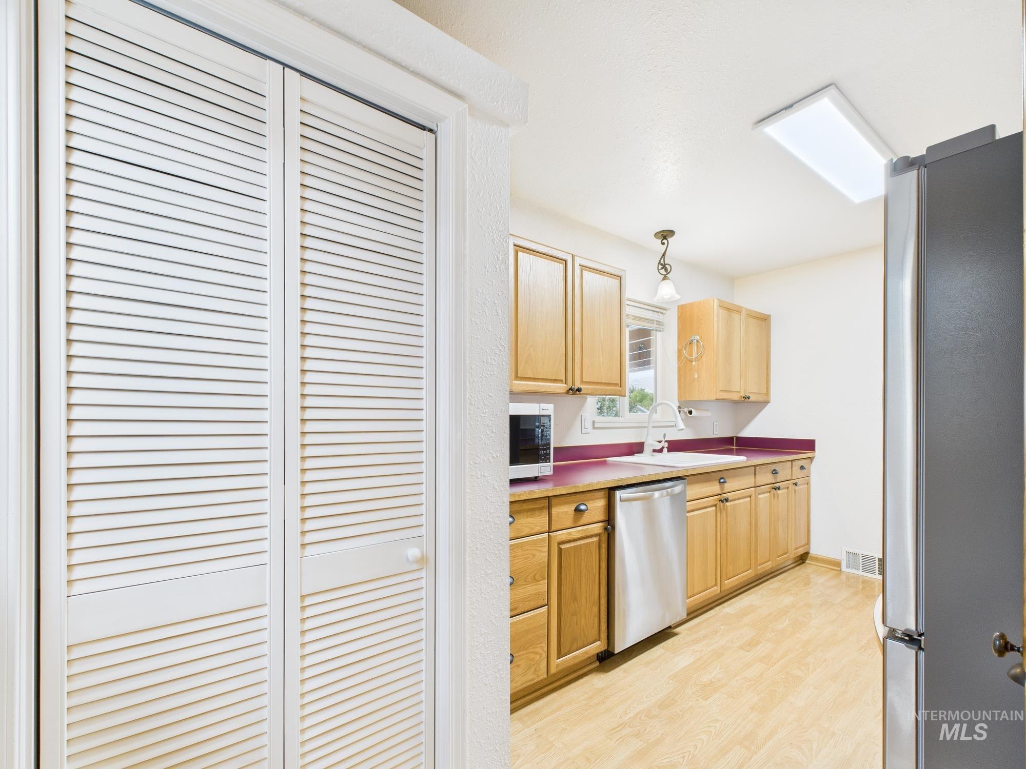 Kitchen with appliances with stainless steel finishes, light wood-style floors, light brown cabinetry, and hanging light fixtures