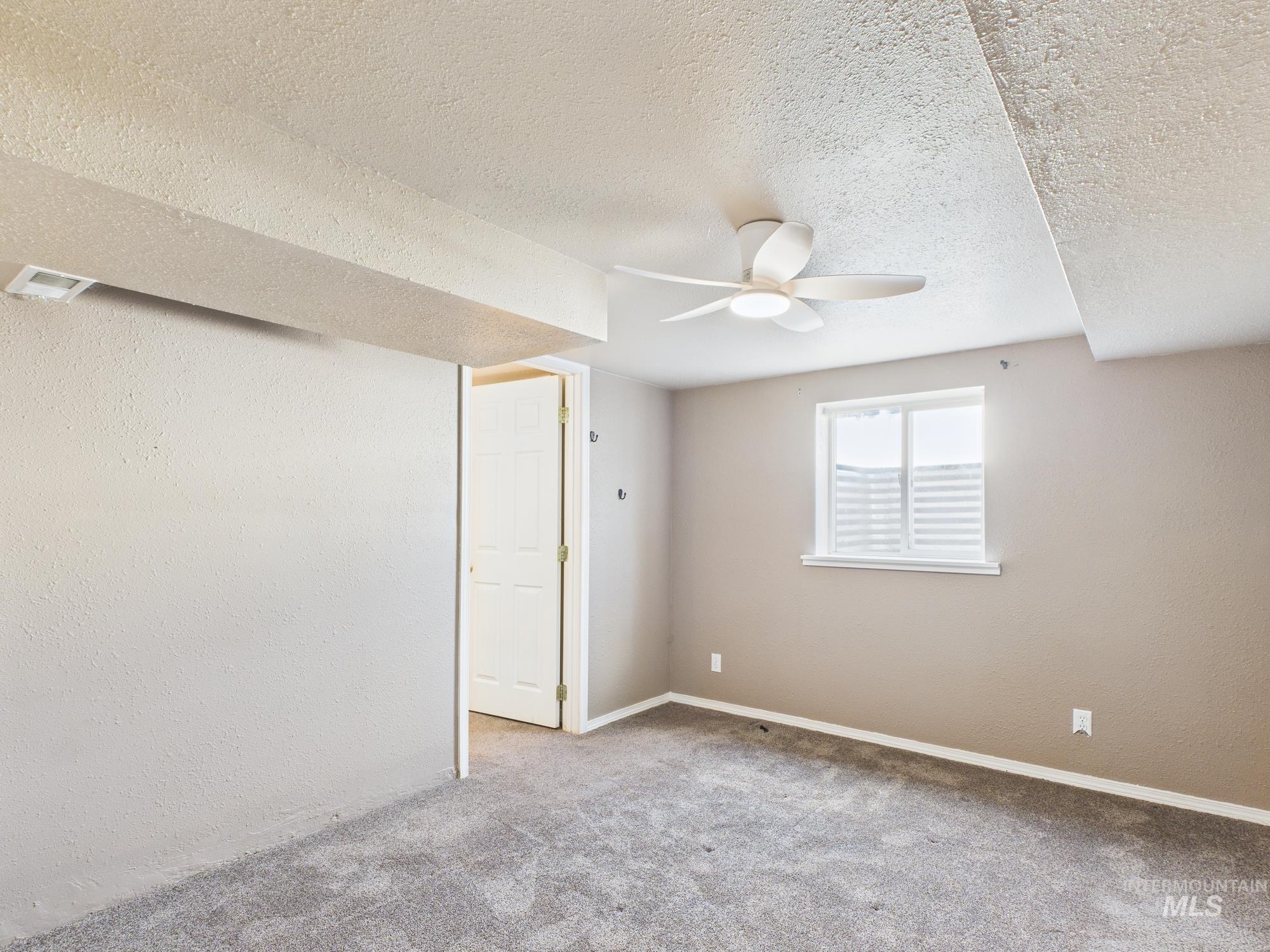 Carpeted empty room with a textured wall, a ceiling fan, and a textured ceiling