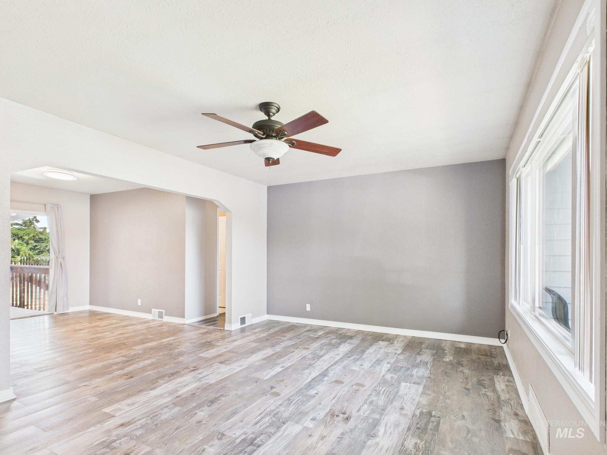 Empty room with light wood-style flooring, arched walkways, and ceiling fan