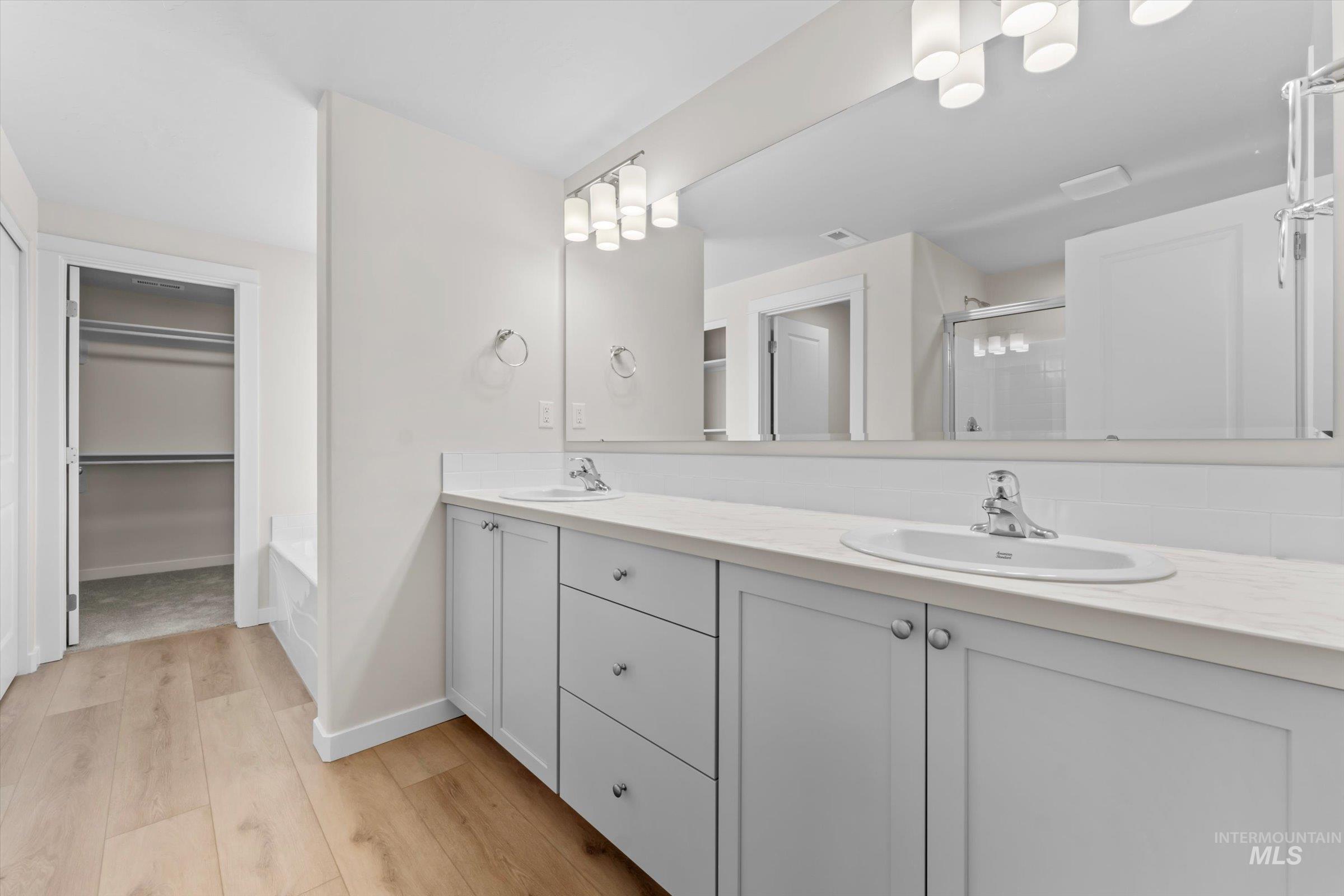 Full master bathroom featuring a spacious closet, a stall shower, light wood finished floors, and double vanity