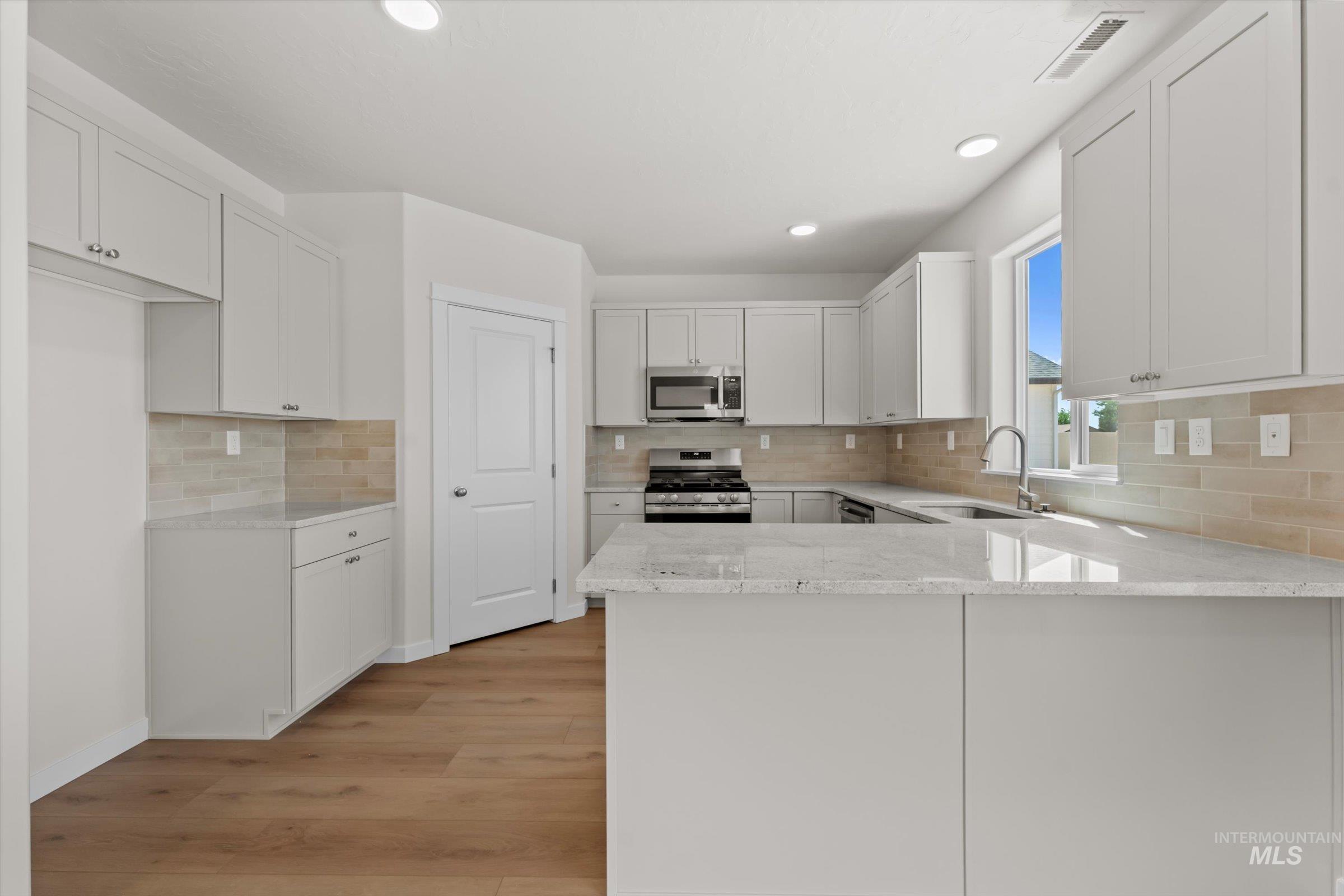 Kitchen featuring a peninsula, light stone countertops, backsplash, white cabinets, and recessed lighting