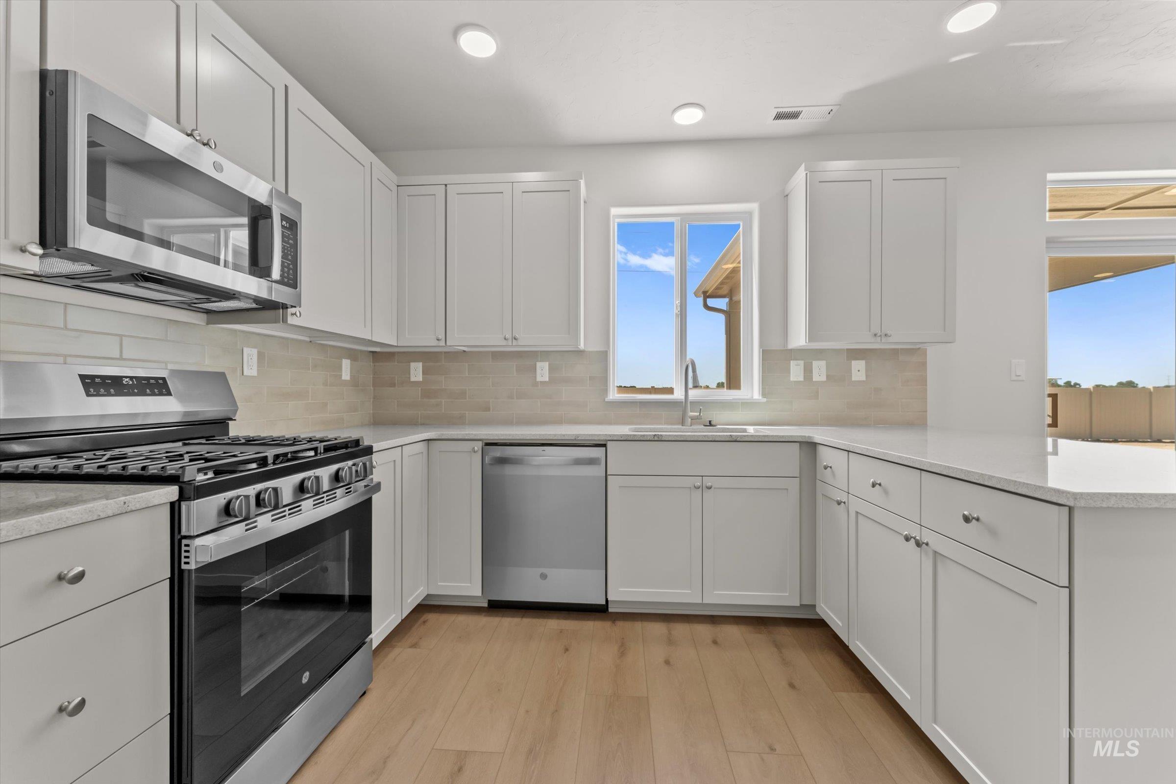 Kitchen featuring appliances with stainless steel finishes, light wood-type flooring, white cabinetry, light stone countertops, and backsplash