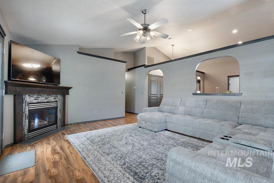 Living area with arched walkways, light wood-style flooring, a glass covered fireplace, a ceiling fan, and high vaulted ceiling