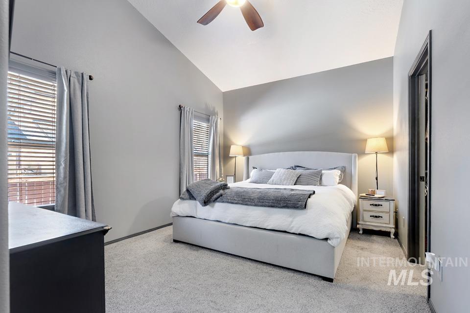 Bedroom with light colored carpet, ceiling fan, and high vaulted ceiling