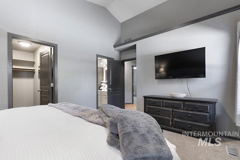 Bedroom featuring a walk in closet, light colored carpet, high vaulted ceiling, and ensuite bath