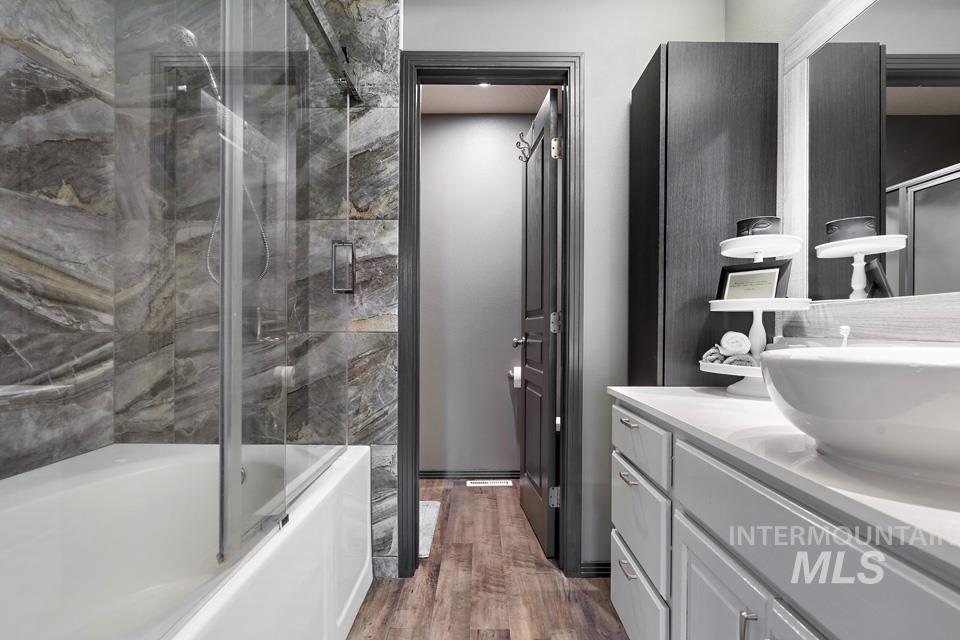 Bathroom featuring vanity, shower / bath combination with glass door, and dark wood finished floors