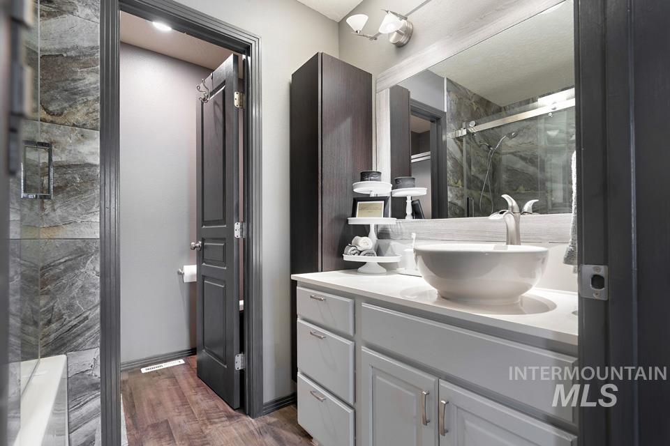 Full bathroom with a marble finish shower, vanity, and dark wood finished floors