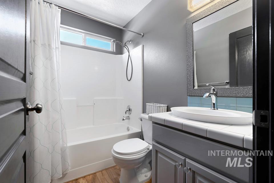 Full bath featuring shower / tub combo with curtain, light wood finished floors, vanity, and a textured ceiling
